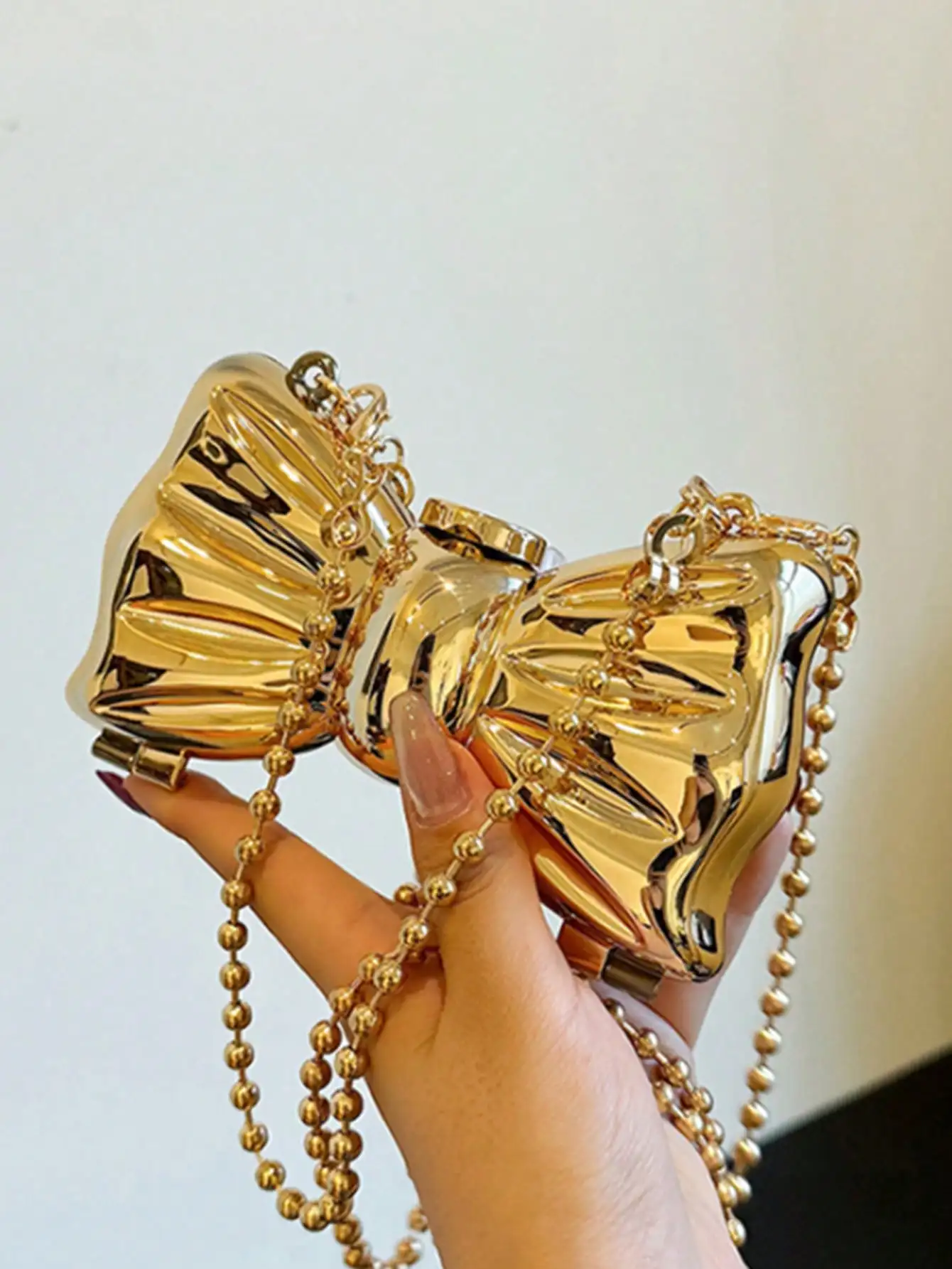 Золотистый металлический вечерний клатч в форме банта с жестким корпусом и ремешком из шариковой цепочки
Золотистый металлический вечерний клатч в форме банта с жестким корпусом и ремешком из шариковой цепочки