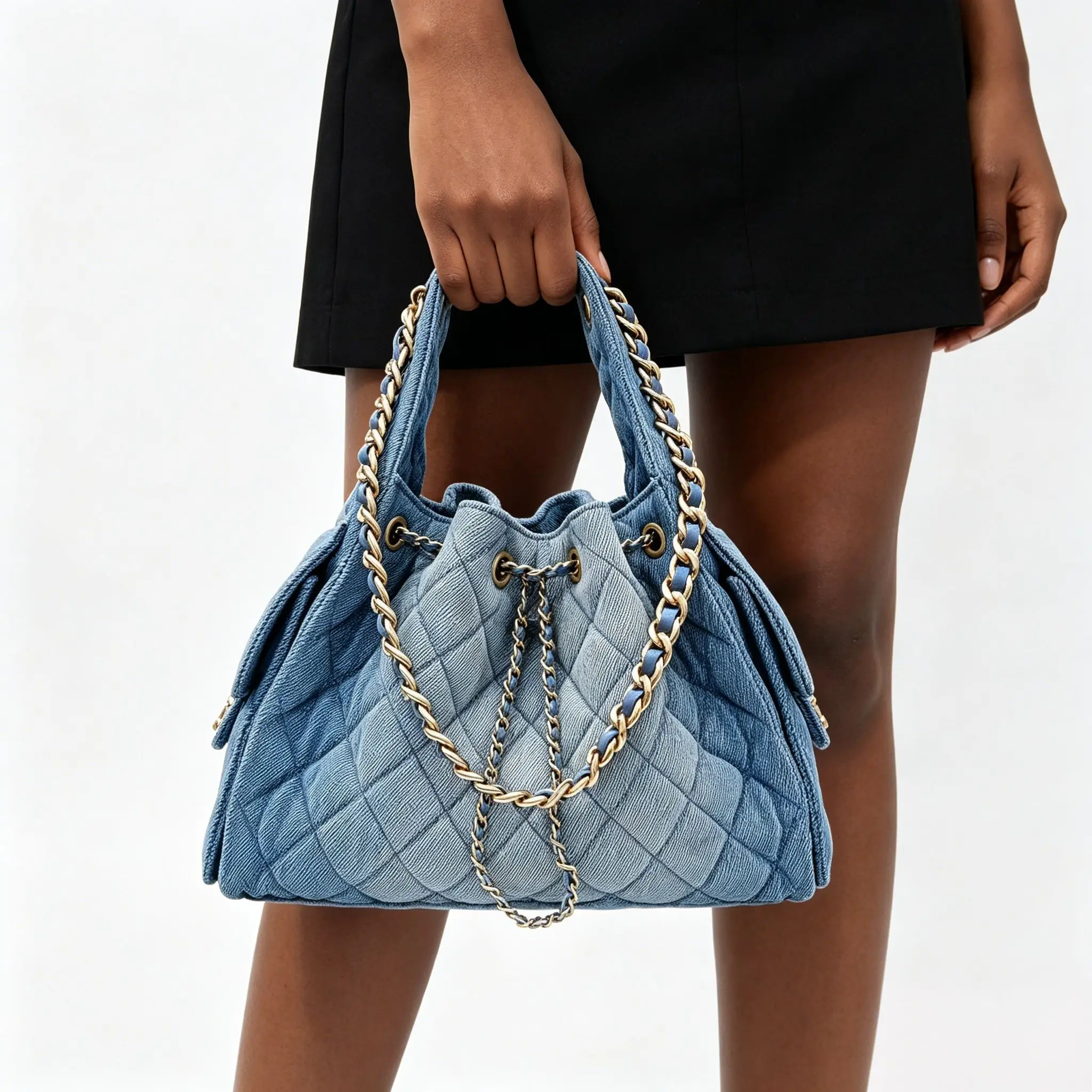Casual-chic bucket bag crafted from quilted light blue denim, featuring a drawstring closure and a leather-woven gold chain strap.
Casual-chic bucket bag crafted from quilted light blue denim, featuring a drawstring closure and a leather-woven gold chain strap.
