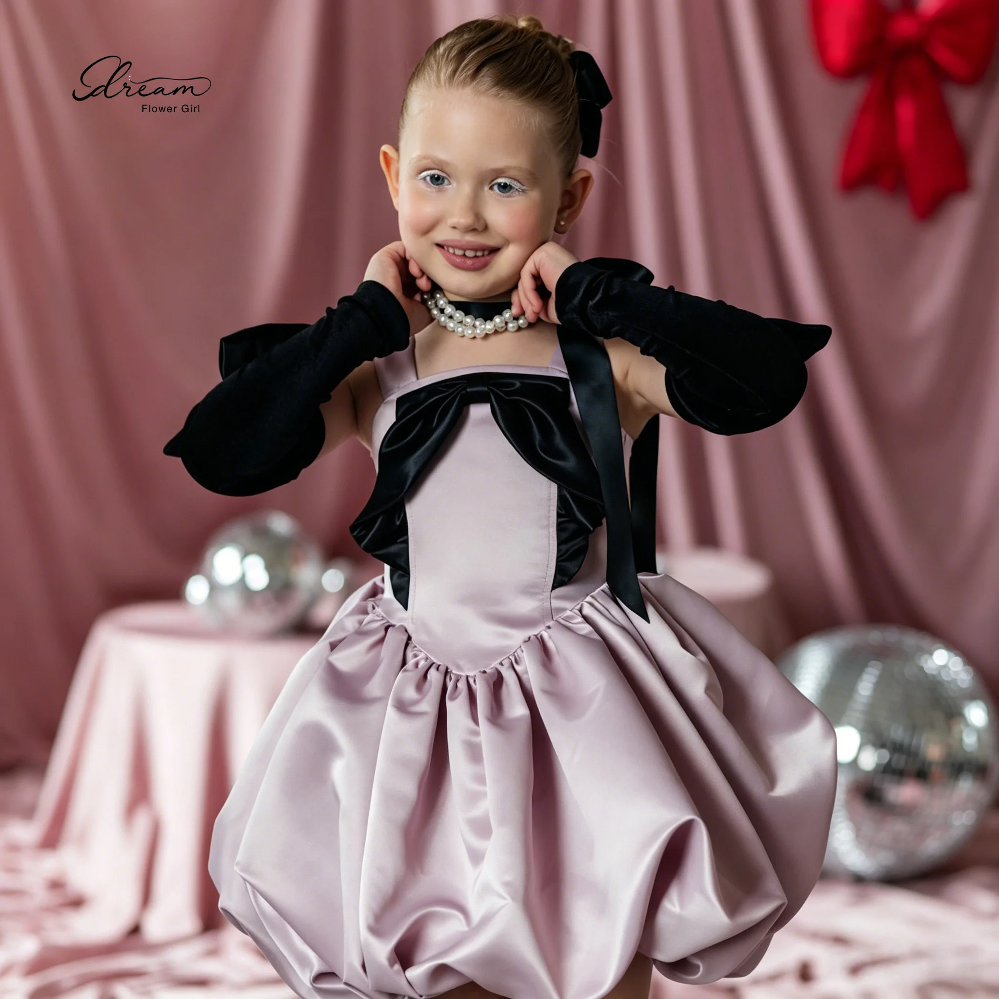 Pink princess-style formal dress for girls featuring a puffy skirt spaghetti straps, and a black bow accent on the bodice
Pink princess-style formal dress for girls featuring a puffy skirt spaghetti straps, and a black bow accent on the bodice