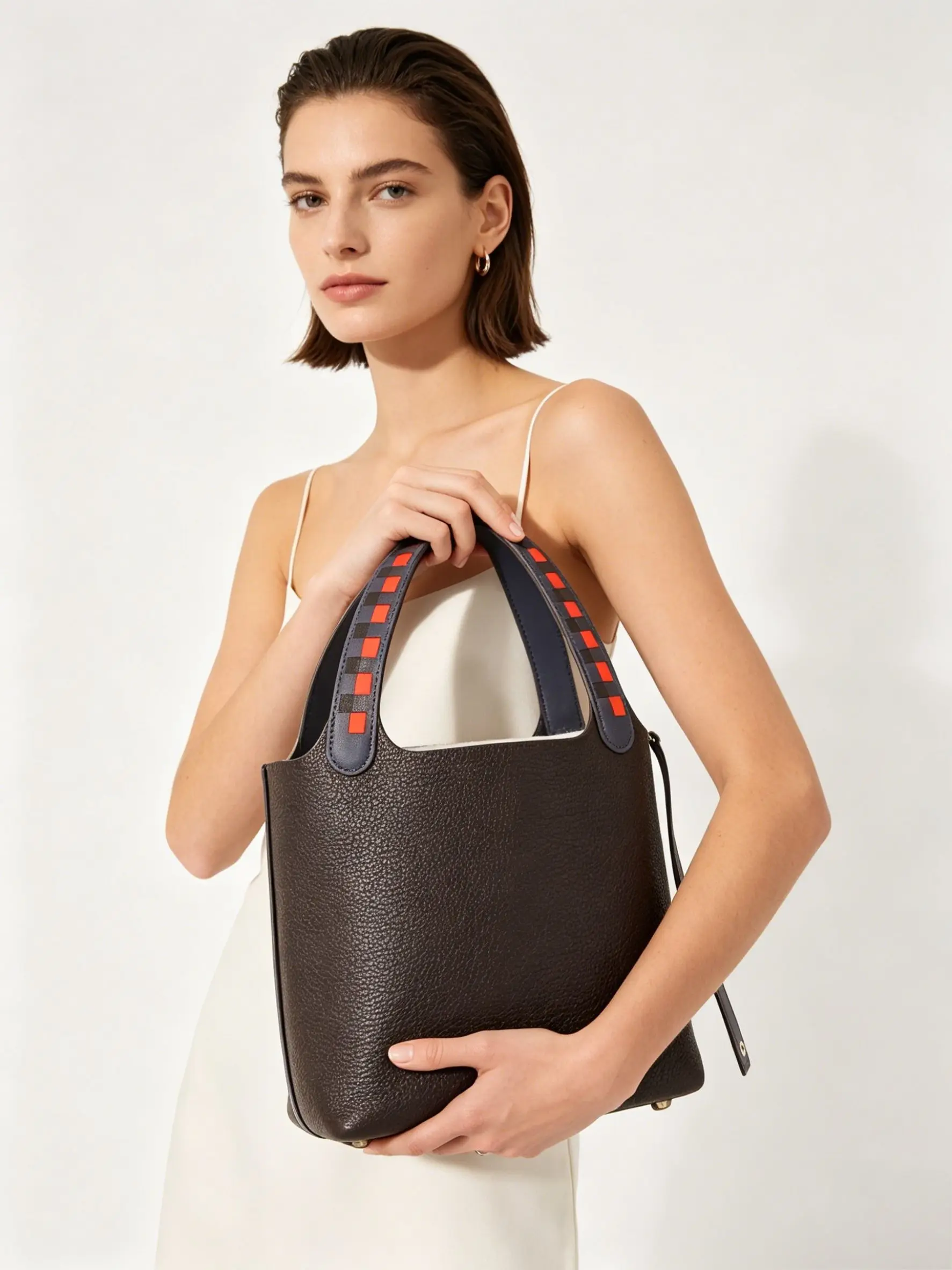 The handbag is made of high-quality dark brown pebbled leather, featuring a unique color-block handle and a spacious bucket design.
The handbag is made of high-quality dark brown pebbled leather, featuring a unique color-block handle and a spacious bucket design.