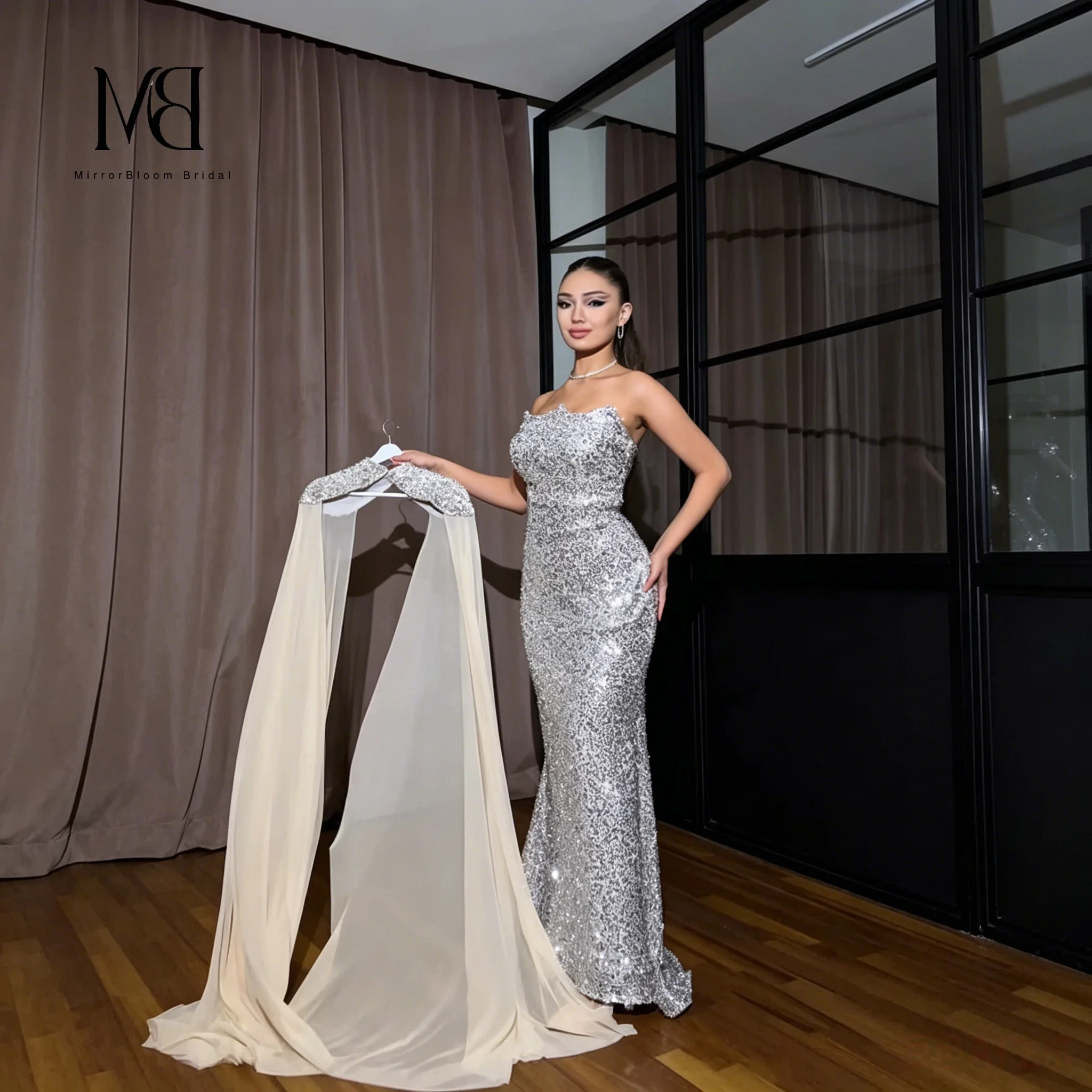 Exquisite silver strapless sleeveless floor-length mermaid formal gown featuring sequin detailing and a floor-length cape
Exquisite silver strapless sleeveless floor-length mermaid formal gown featuring sequin detailing and a floor-length cape
