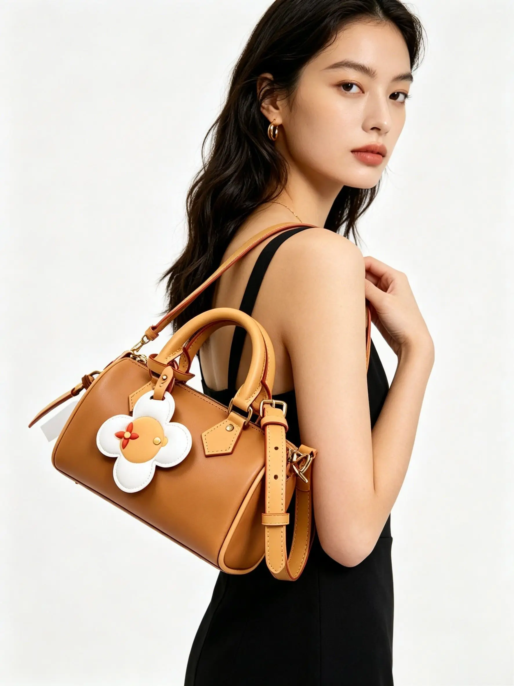 Tan leather mini barrel bag with a playful flower charm, dual top handles, and a detachable crossbody strap.
Tan leather mini barrel bag with a playful flower charm, dual top handles, and a detachable crossbody strap.