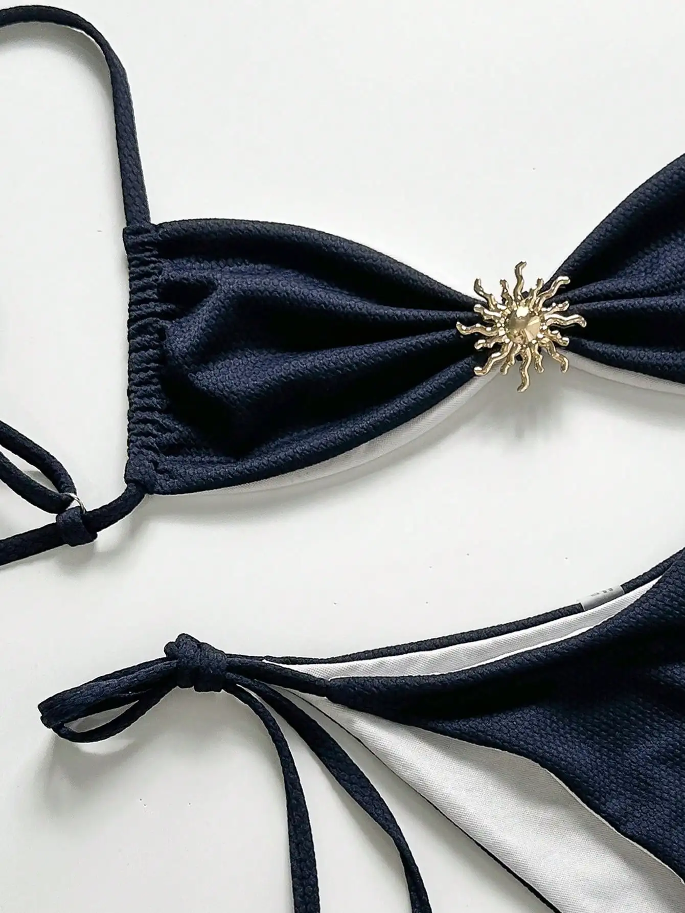 Женский однотонный текстурированный комплект бикини темно-синего цвета с металлическим декором в виде солнечного кулона, завязками сбоку и открытой спиной
Женский однотонный текстурированный комплект бикини темно-синего цвета с металлическим декором в виде солнечного кулона, завязками сбоку и открытой спиной