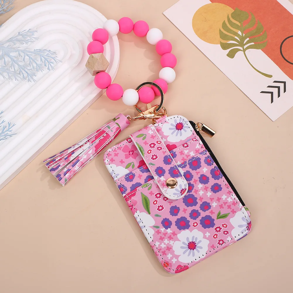 La pulsera de silicona con tarjetero es un accesorio de viaje esencial para estudiantes, trabajadores de oficina y madres amables. Se puede fijar de forma segura en la muñeca, liberando tus manos para un viaje diario más relajado. El diseño floral fresco combinado con cuentas de madera coloridas y detalles de borlas lo convierte en un práctico tarjetero que puede contener tarjetas de campus, tarjetas de autobús, tarjetas bancarias y monedas, y también un elegante accesorio para la muñeca que puede complementar tu atuendo. Es perfecto para la clase, el trabajo, el cuidado de los niños y las compras.