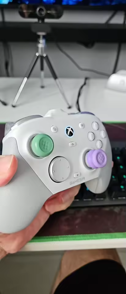 Mão segurando o controle GameSir G7 Pro branco com analógicos customizados em verde e roxo