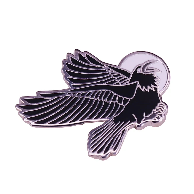 This hard enamel pin depicts a black bird's flight across the of the moon.