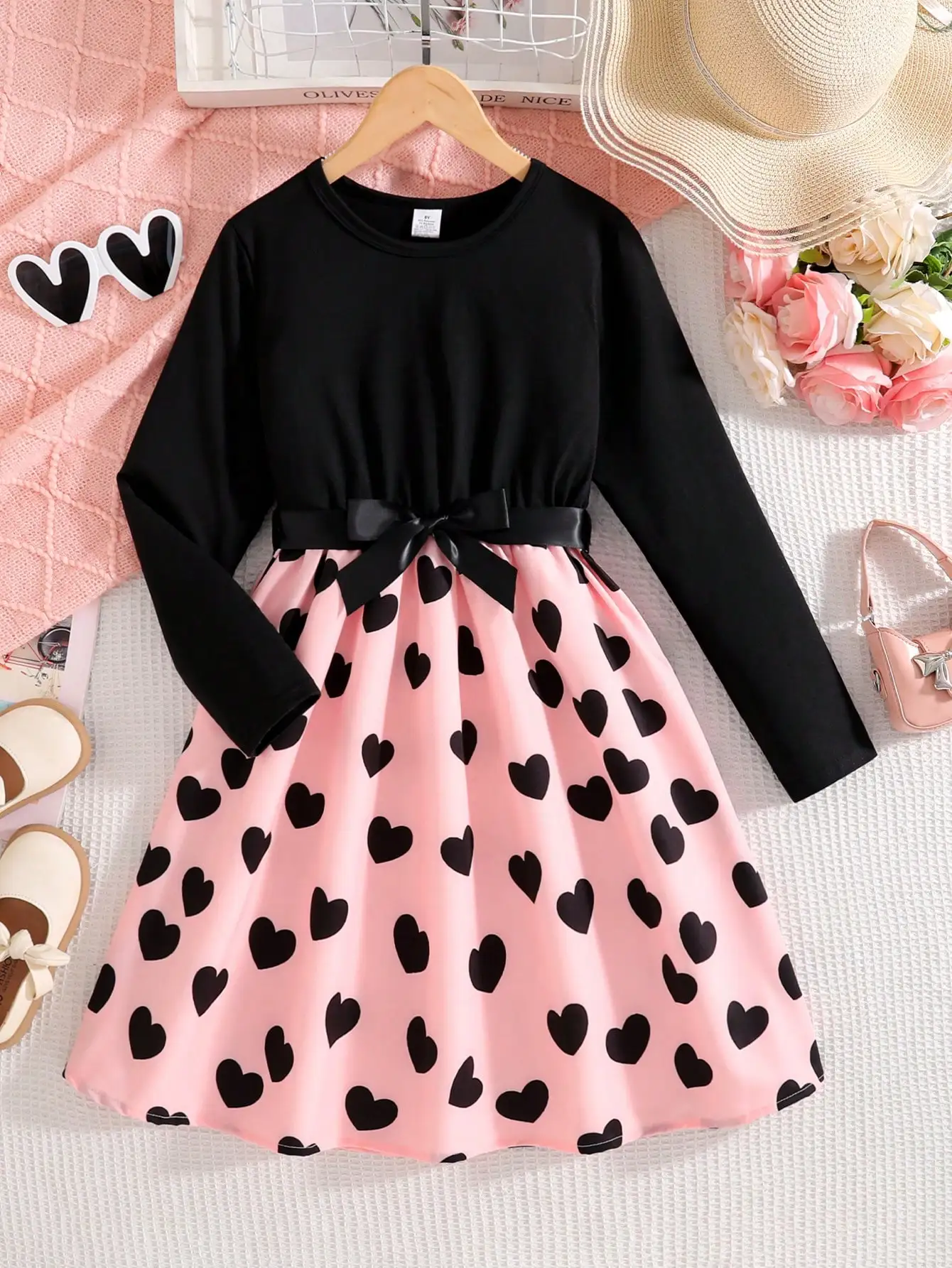 

Женское черное платье с длинными рукавами и круглым вырезом, с розовой юбкой с принтом в виде сердечек и поясом с бантом