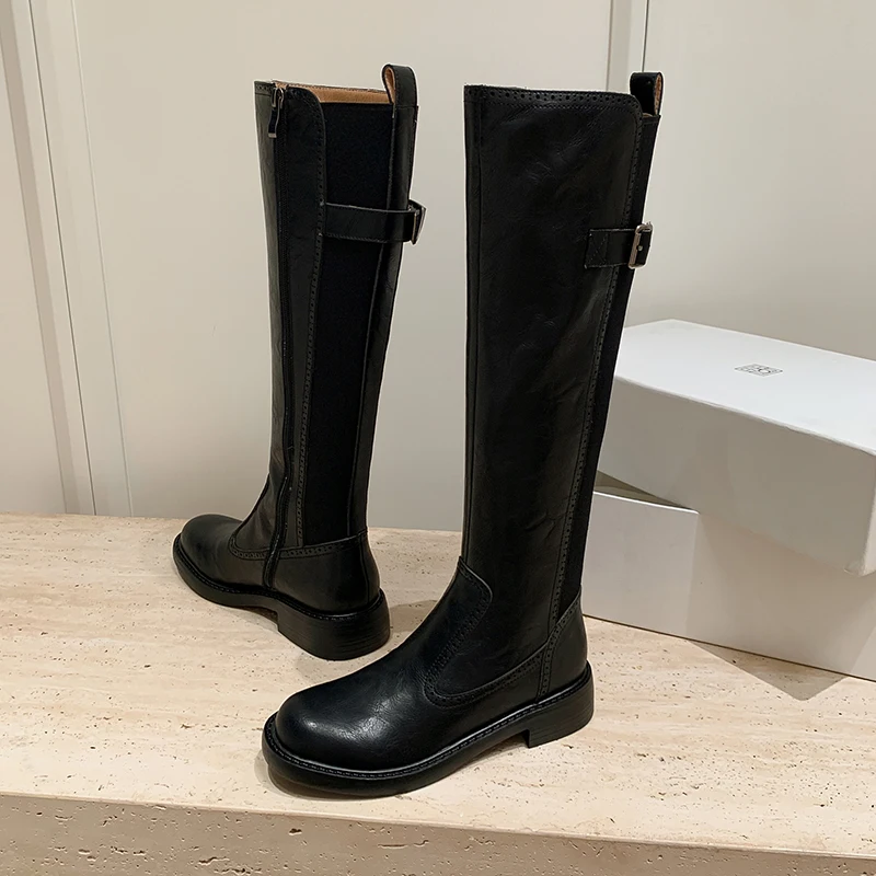 

Современные сапоги до колена из натуральной кожи с круглым носком и пряжкой на ремне. Стильная модная женская обувь.