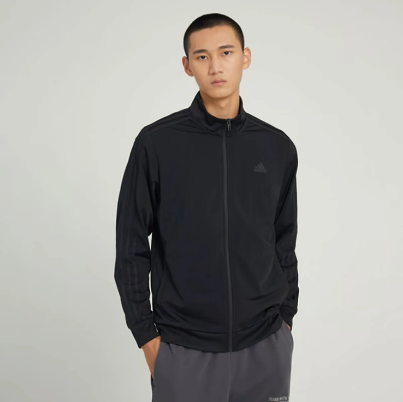 سترة رياضية بسحاب مطبوع عليها شعار الصدر بلون سادة من Adidas ESSENTIALS للرجال باللون الأسود