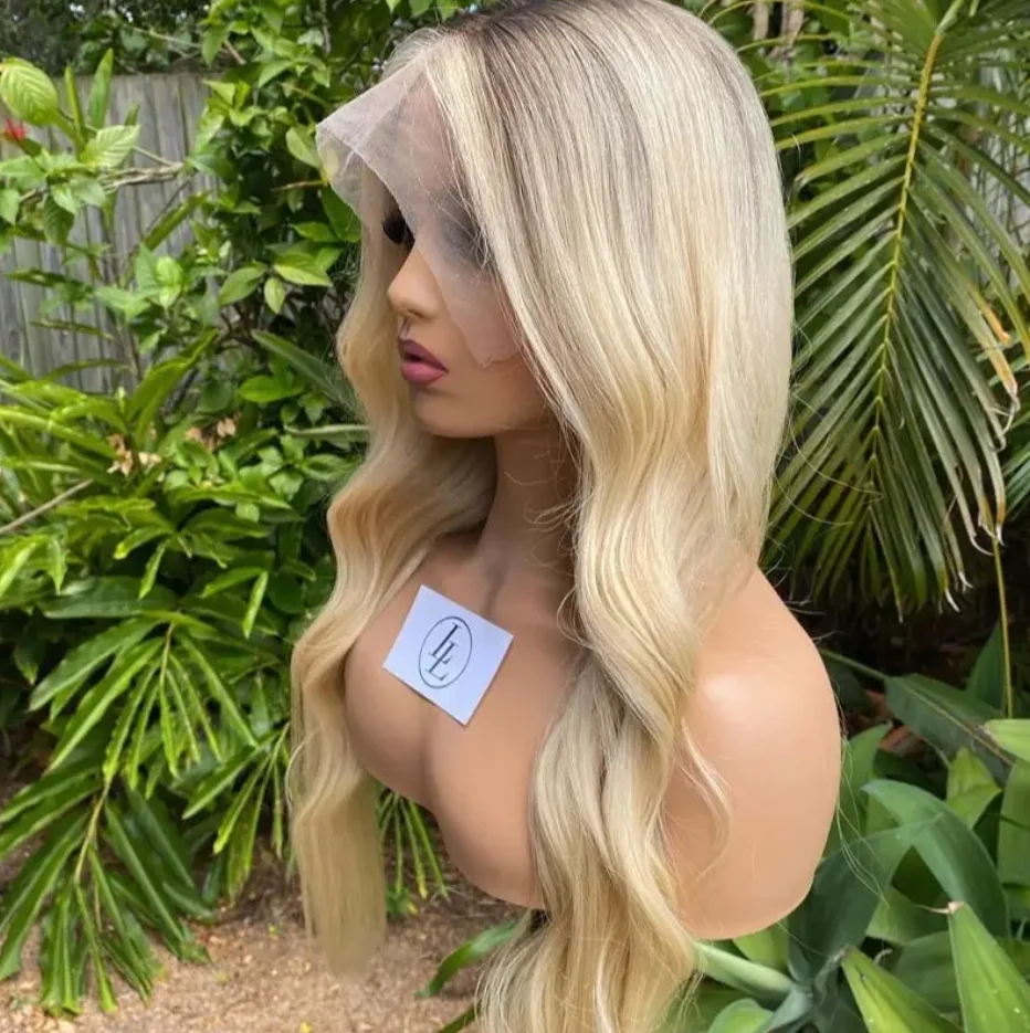 Peruka syntetyczna typu lace front z ciemnymi odrostami, jasnoblondowa peruka, peruka z falą body wave, naturalna peruka falowana, wstępnie wyskubana linia włosów, blond peruka z miękką koronką.
