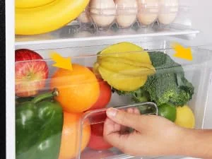 eine Person, die nach einem Plastikbehälter mit Obst und Gemüse greift.