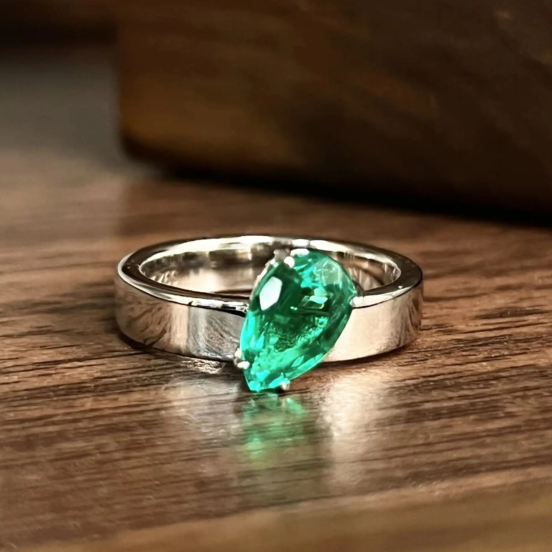S925 sterling silver drop-shaped ring with 1.5 carats of cultured wood-tone green emeralds. Features wide band design.