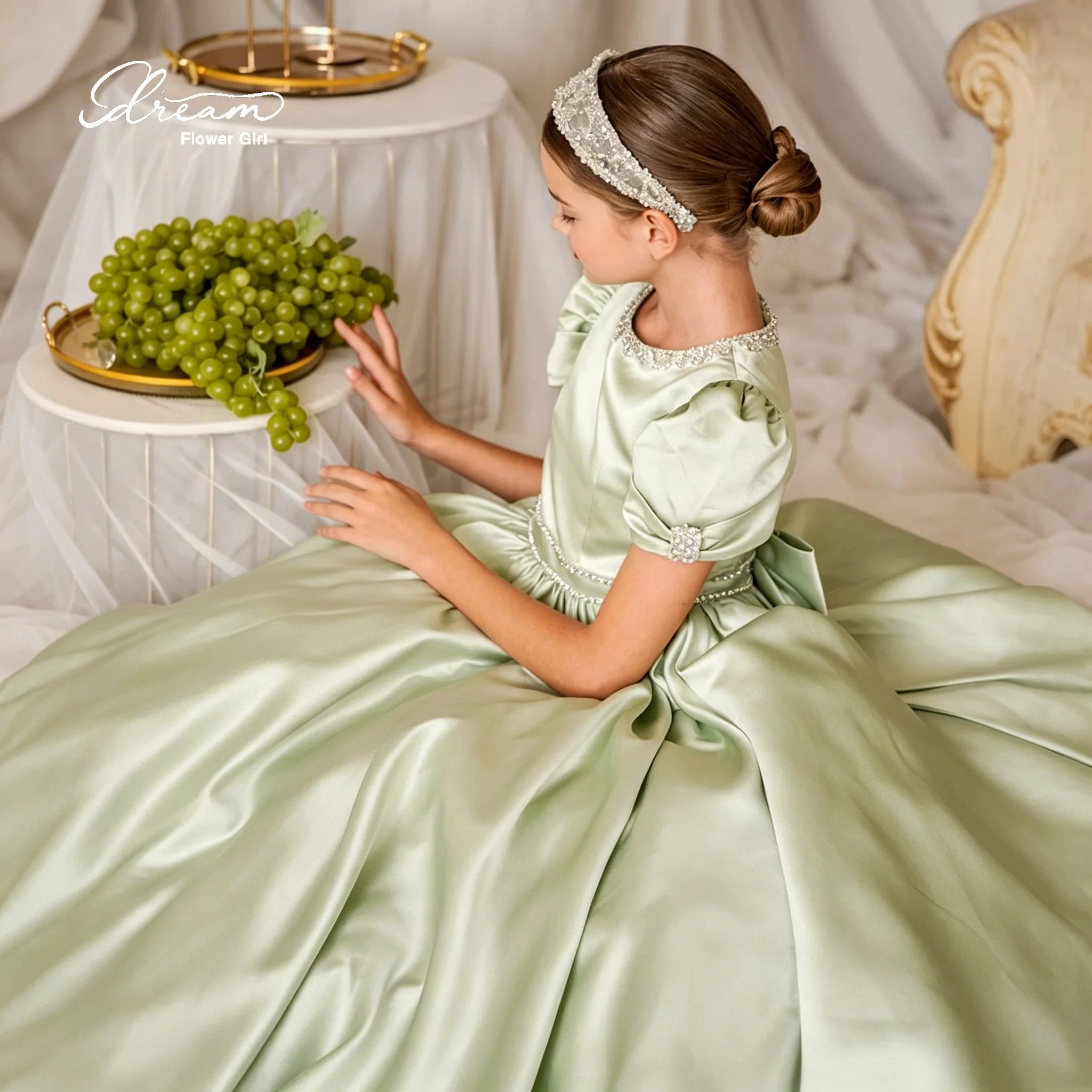 A green satin trailing flowered skirt dress with a flowing hem, featuring a cascading waist design and adorned with bows.