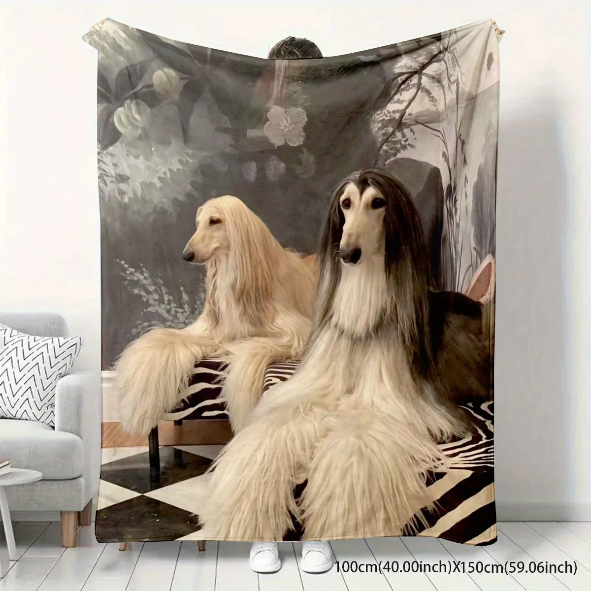 A soft, warm fleece throw blanket featuring a detailed retro artistic print of two long-haired Afghan Hound dogs against a vintage dark floral background, shown draped on a couch and laid over a bed in a home setting.