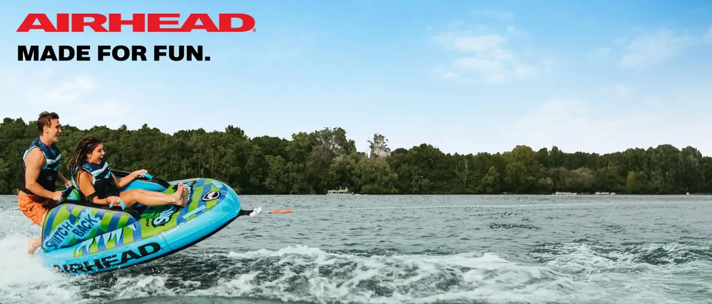 Two people riding an inflatable towable tube behind a boat on a lake on a sunny day.