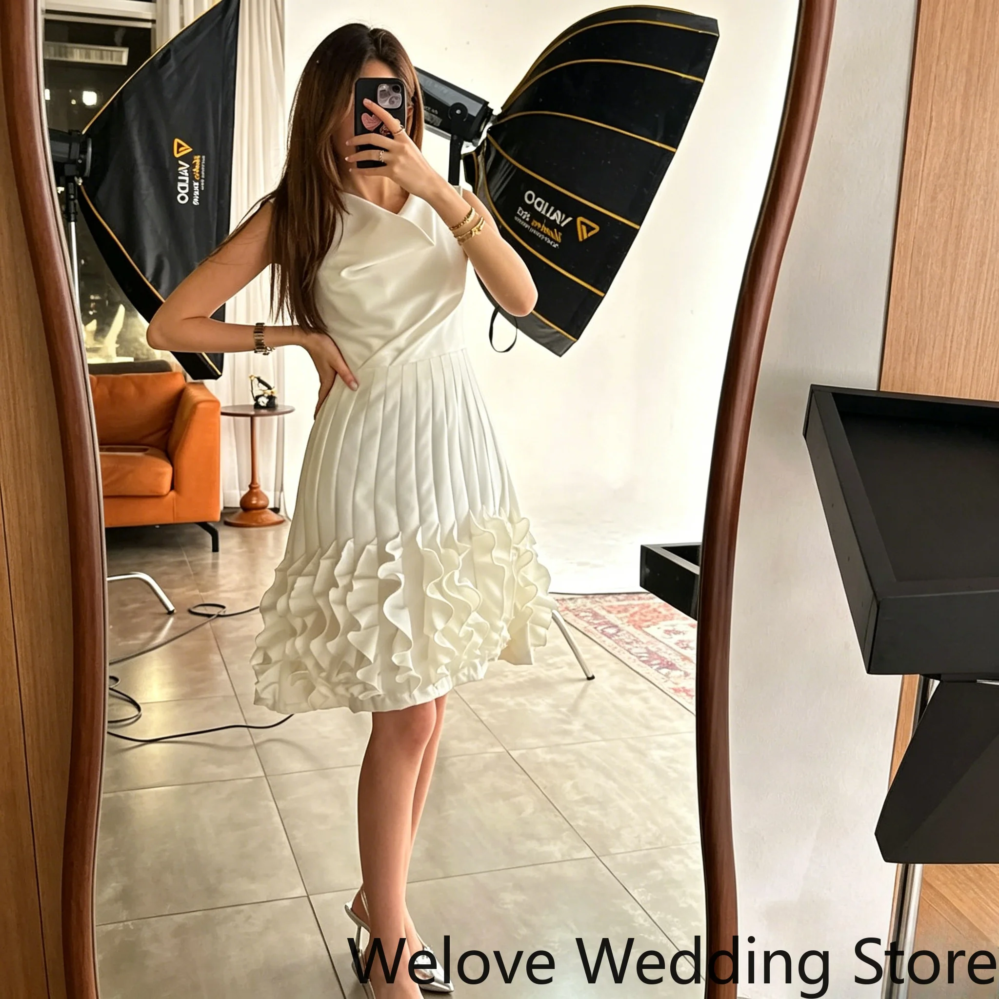 

minimalist white knee‑length formal with draped cowl neckline sleeveless design vertical pleated skirt and layered ruffle hem