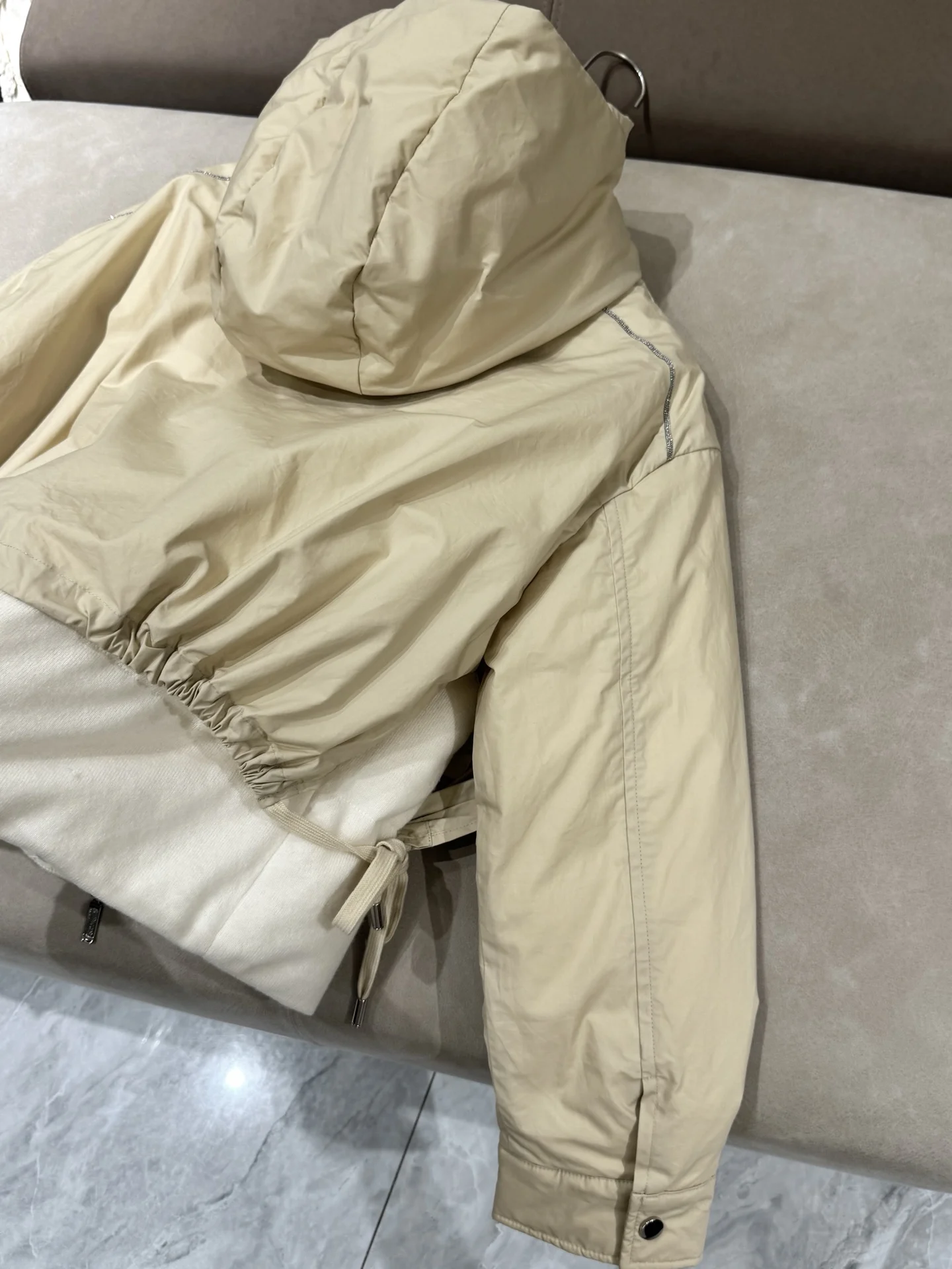 เสื้อแจ็คเก็ตขนเป็ดผสมแคชเมียร์ ขนสัตว์ และผ้าไหม พร้อมฮู้ด แต่งโซ่ประดับลูกปัด และแขนเสื้อแบบดรอปชอลเดอร์ เพื่อทรงสวยสง่า