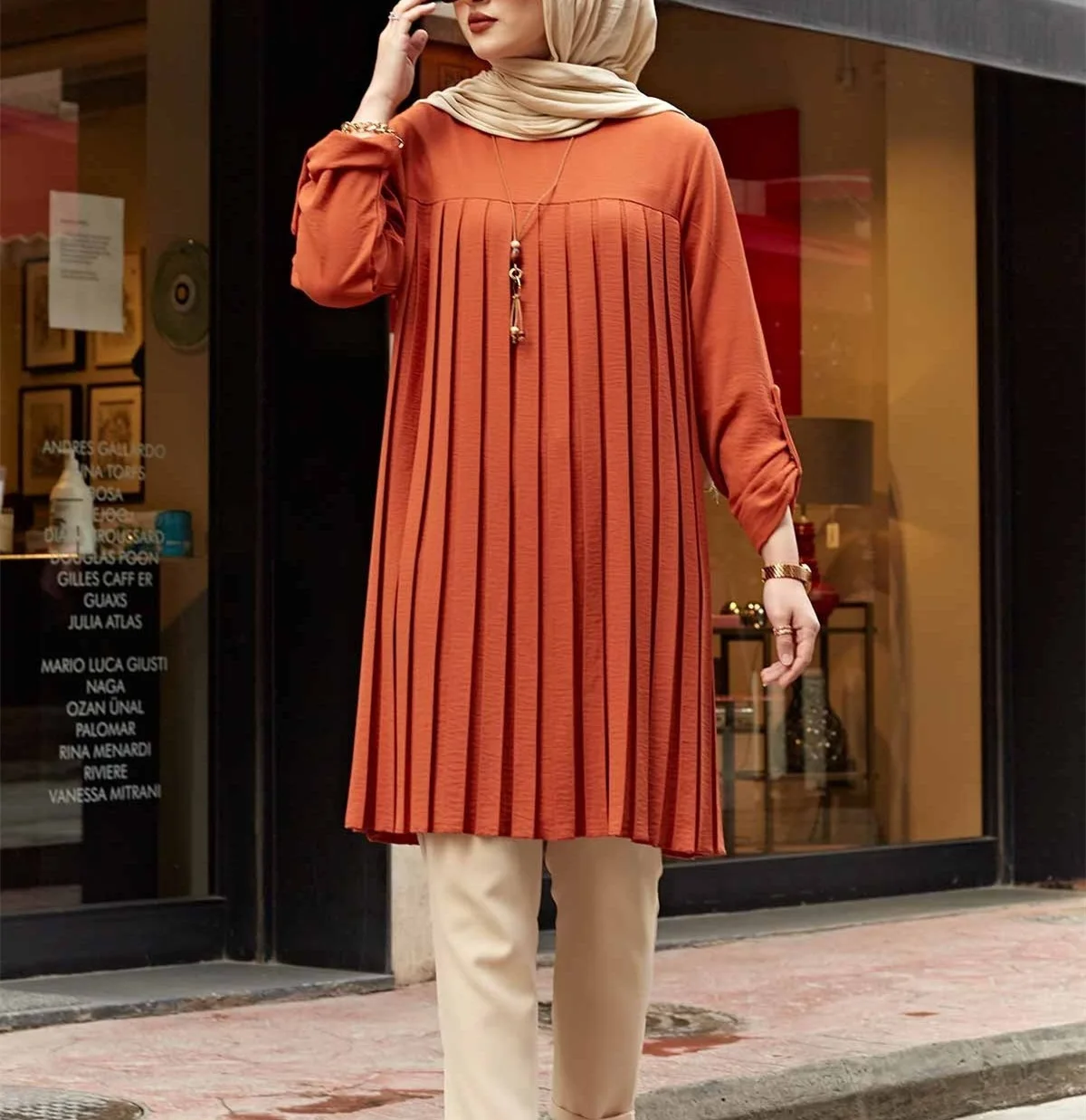 Rust-colored pleated longline tunic with rolled sleeves styled with beige trousers and a headscarf
