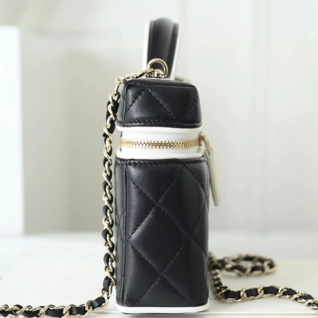 

Black quilted leather vanity bag, white contrast trim, short top handle, gold double zipper, interwoven chain strap.