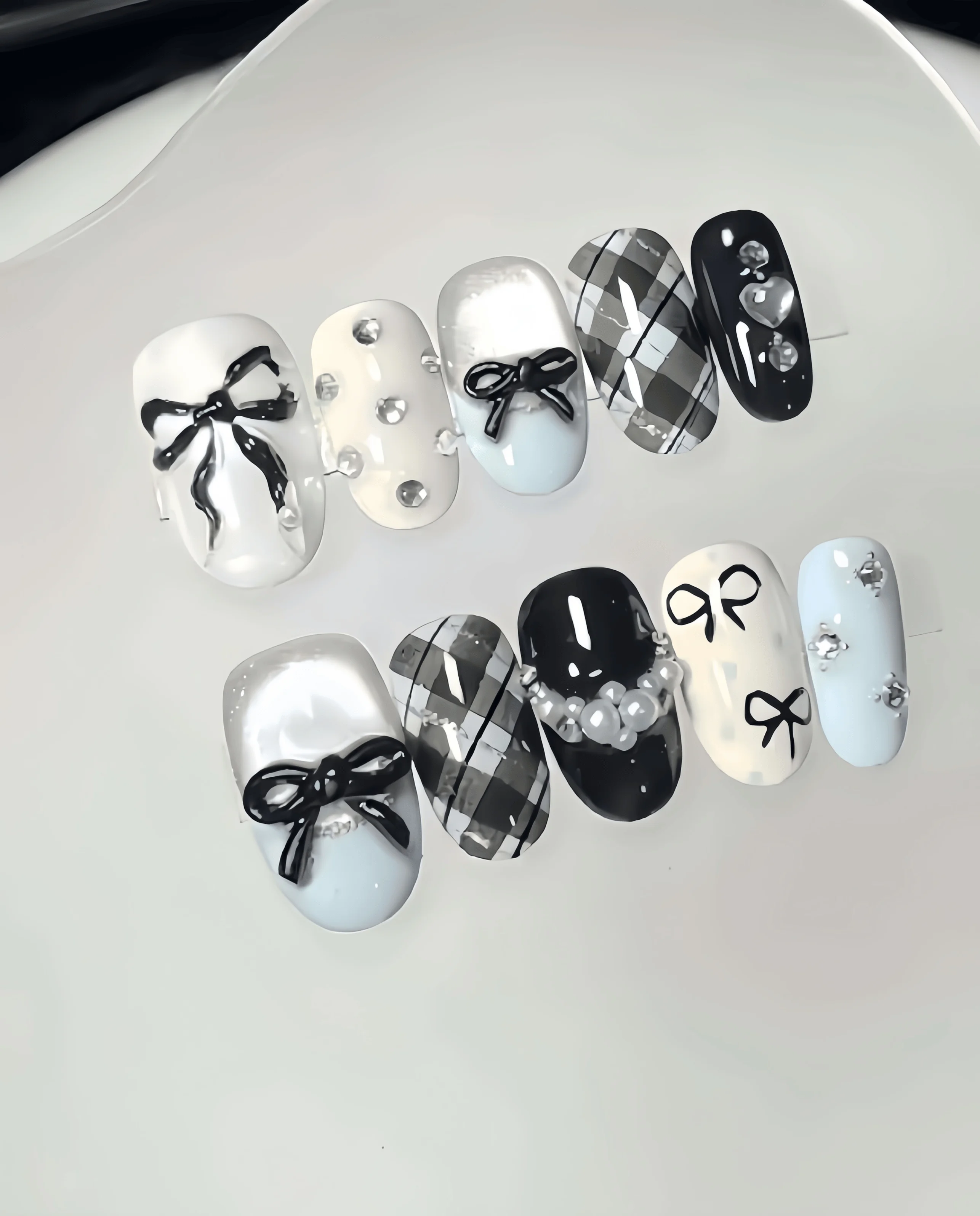 10 faux ongles faits à la main en forme d'amande, longueur moyenne, en combinaisons de couleurs blanc laiteux, bleu clair et noir à carreaux, avec décorations nœuds peints à la main, perles et strass en forme de cœur, dans un style collégien doux et cool, adaptés aux femmes et aux filles, parfaits pour les vacances d'été, la saison des diplômes et comme cadeau, livrés avec 1 colle gelée et 1 lime à ongles.