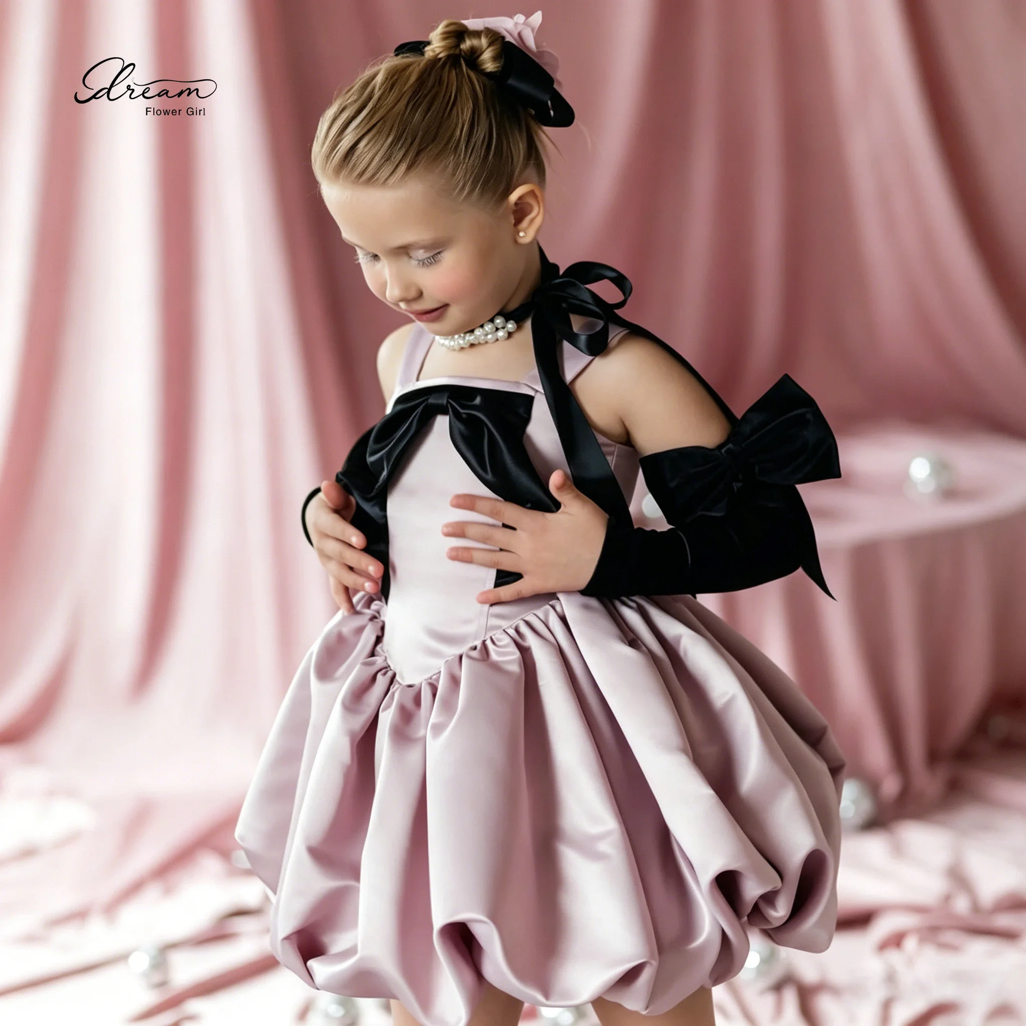Pink princess-style formal dress for girls featuring a puffy skirt spaghetti straps, and a black bow accent on the bodice