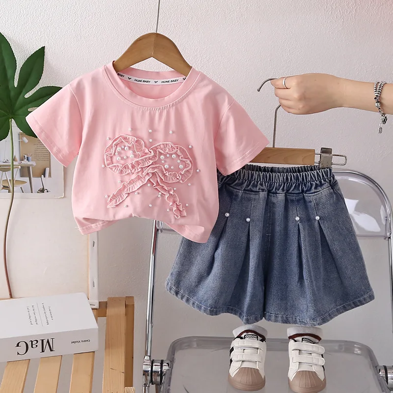 

Комплект для девочек: футболка с кружевом, бантом и жемчугом, короткий рукав + джинсовая юбка. Новинка лета 2026. Модный повседневный наряд в стиле милой принцессы.