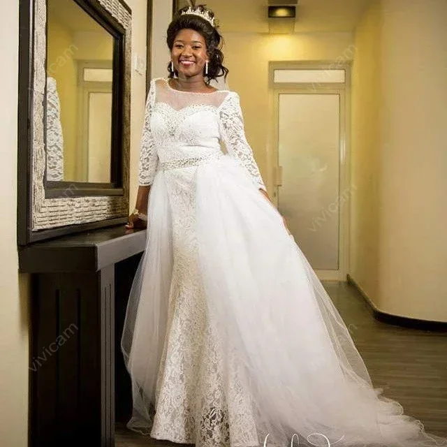 Suknie ślubne z koronką, dekoltem w łódkę, długimi rękawami, odpinanym trenem i odkrytymi plecami, zdobione uroczy, personalizowane kryształki.