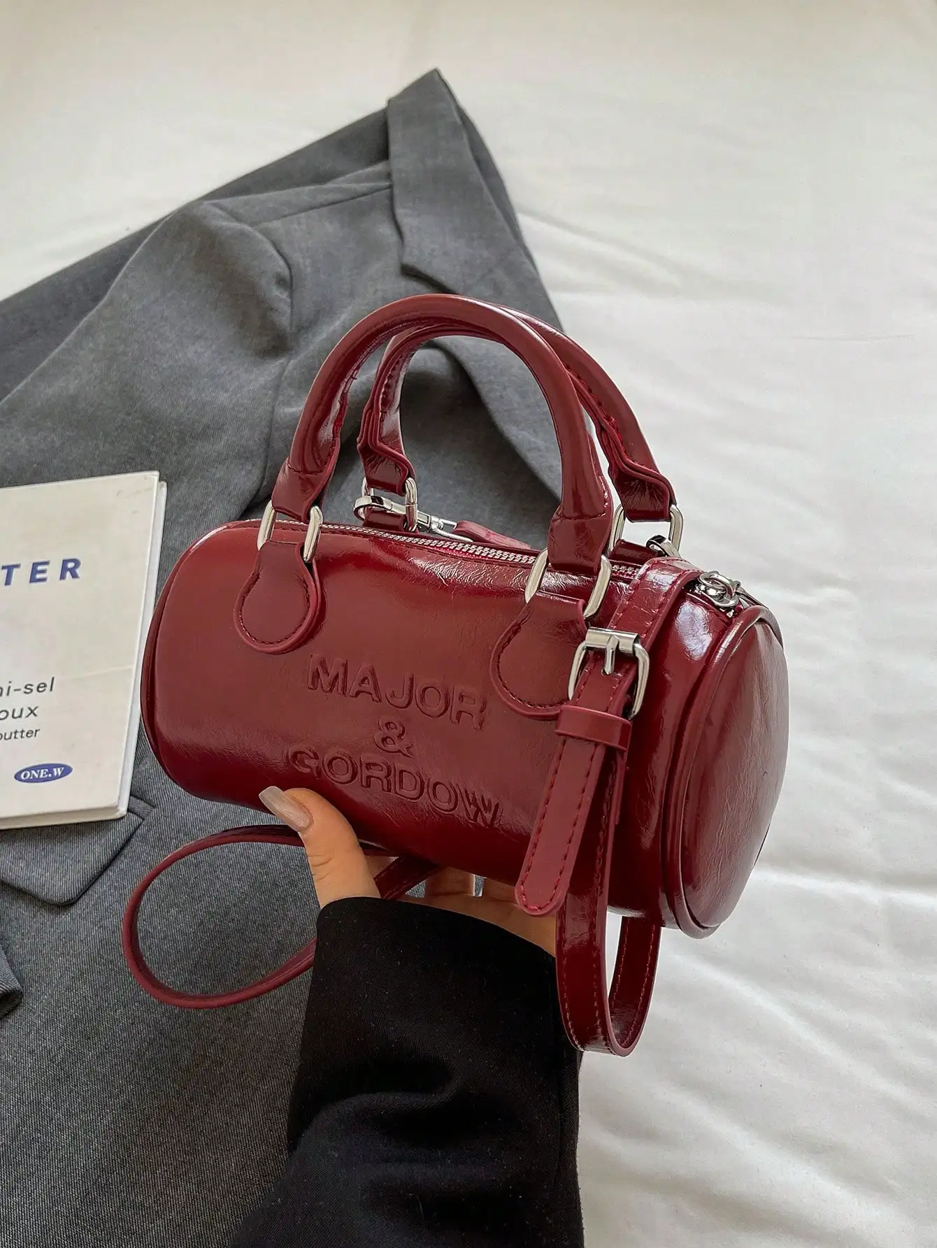 

Глянцевая красная сумка-цилиндр с ручкой и тисненым логотипом, с ремнем для ношения через плечо и на плече