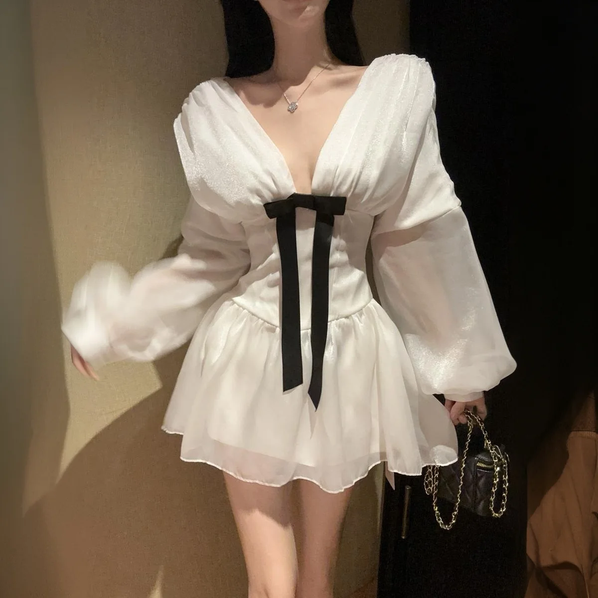 เดรสสั้นสีขาวแบบเซ็กซี่สไตล์ฝรั่งเศส คอวีลึก แต่งโบว์ แขนยาวทรงโคมไฟ ผ้าบาง โชว์เอวเข้ารูป ทรงเอไลน์ เหมาะสำหรับงานวันเกิด