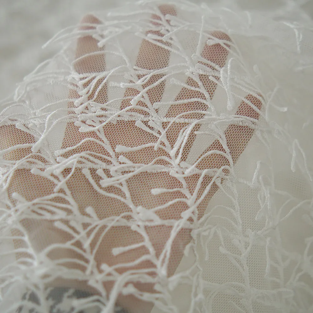 Weißer Spitzenstoff mit Fransen und der strukturierte, netzähnliche Stoff für Hochzeitskleider und formelle Kleider