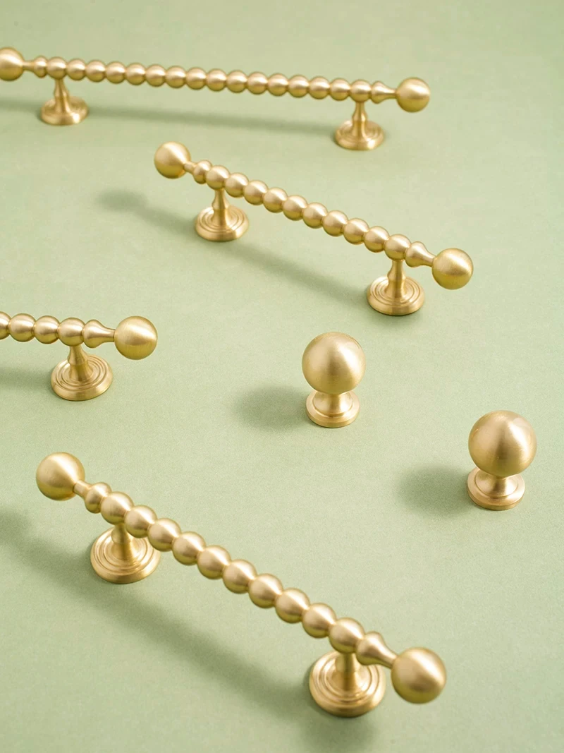 Beaded brass pulls and round knobs on a green background