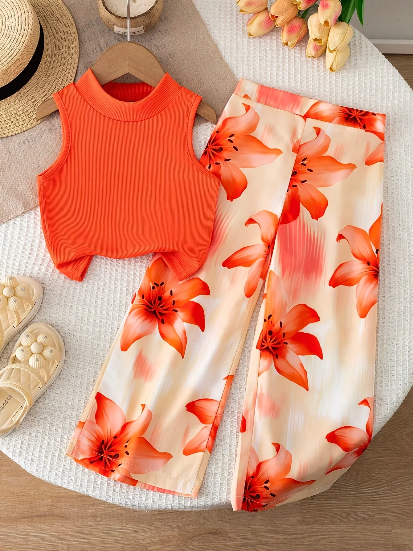 Conjunto de dos piezas estilo vacacional naranja para niñas: top corto sin mangas con cuello simulado, de color liso y textura acanalada, combinado con pantalón fluido con estampado de lirios.