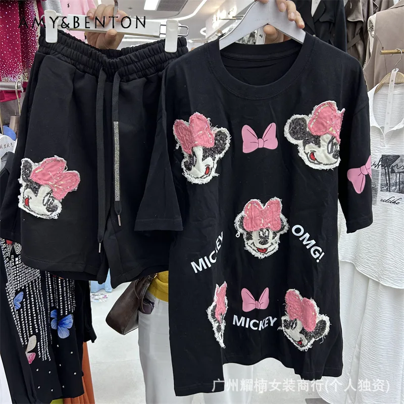 

Женский костюм-двойка: футболка с коротким рукавом, сложным кроем и принтом в виде букв и мультяшных персонажей, а также шорты с широкими штанинами на эластичном поясе.