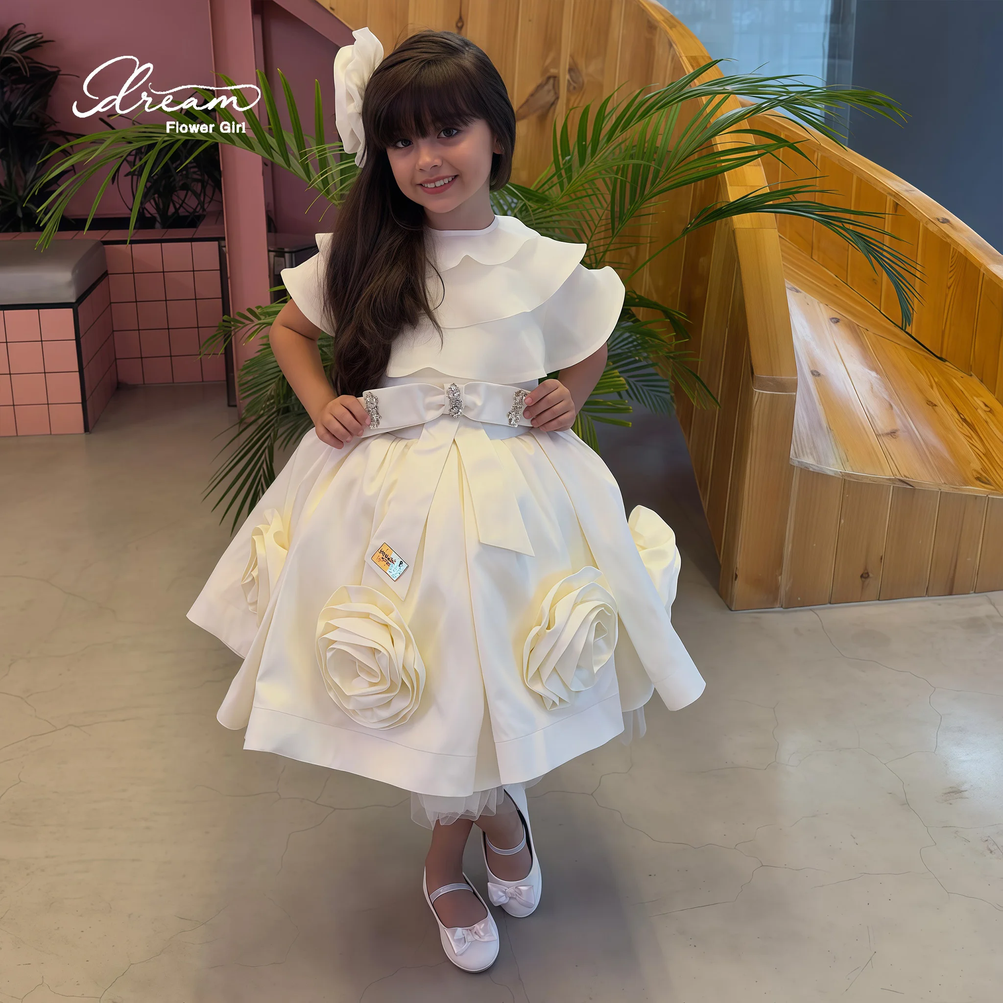 Ivory knee-length formal party dress for girls featuring a high neck ruffled sleeves a voluminous skirt and bow appliqué