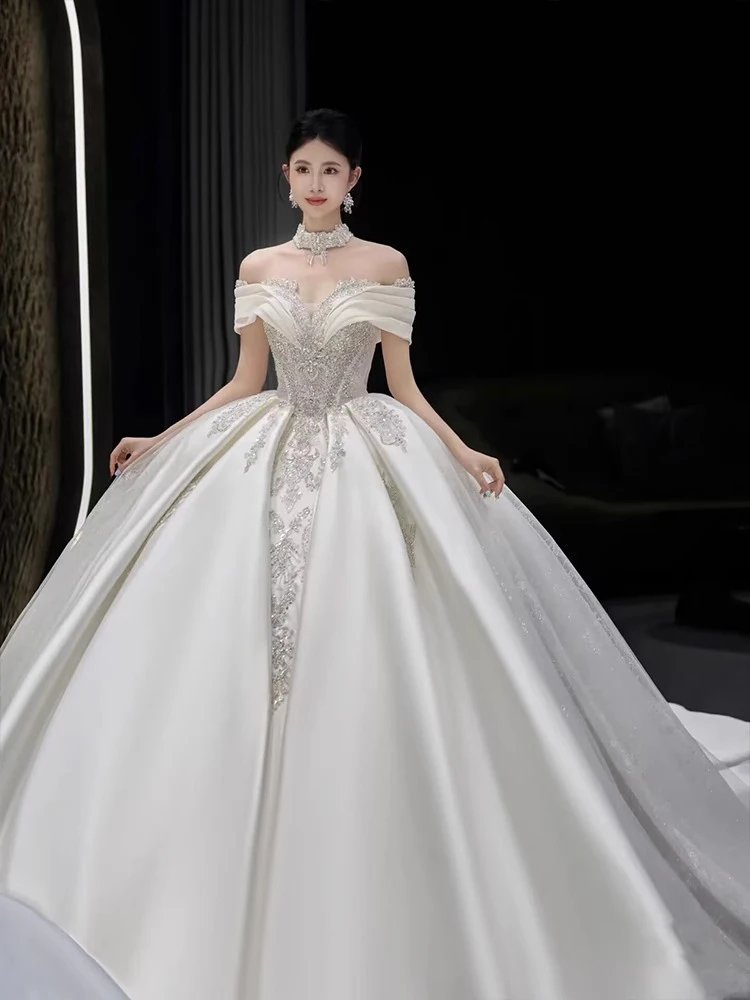 ชุดแต่งงานผ้าซาตินแบบไหล่เดียว ประดับตกแต่งอย่างหรูหรา พร้อมชายกระโปรงยาวแบบสเวปเทรน  ลายมัดย้อมแบบราชวงศ์  ประดับเพชรอะคริลิก  งานปักลายกลางตัวชุด