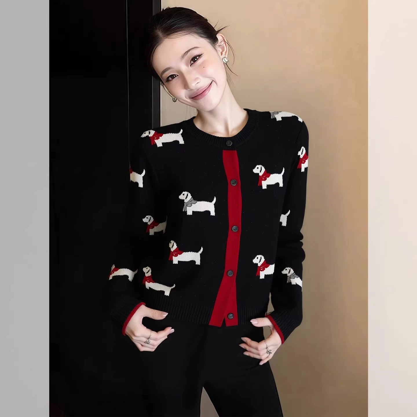 A woman modeling a black women's button-down knitted cardigan featuring a white dachshund dog pattern, long sleeves, and a red front accent trim.