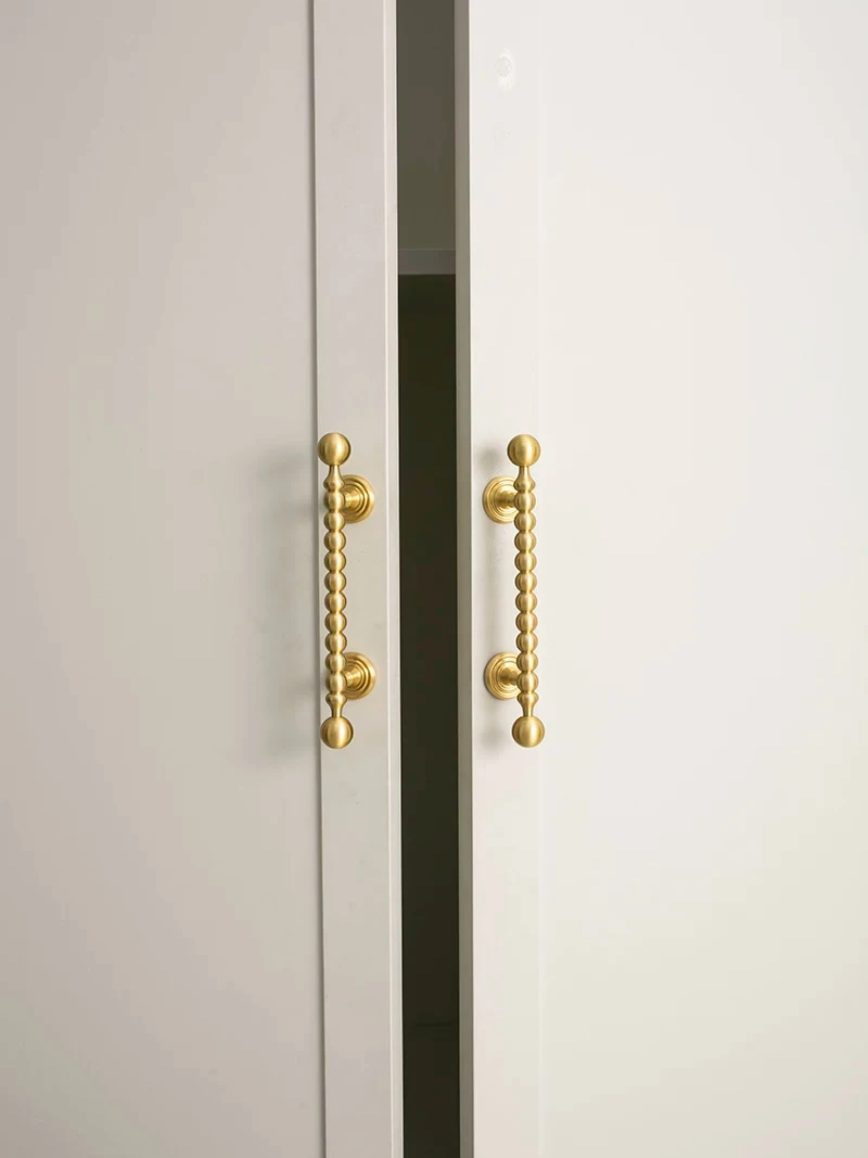 Beaded brass handles fitted to partially open white cupboard doors