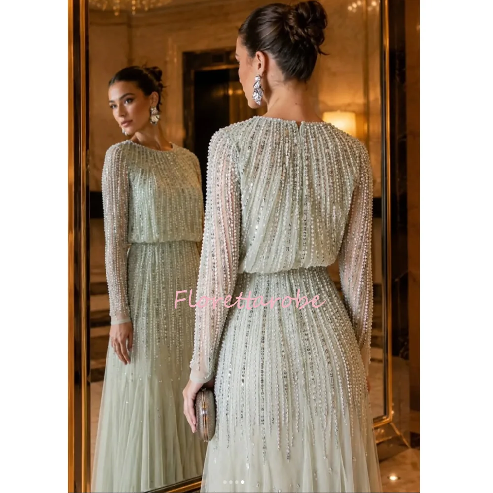 Vestido de noche verde con cuello redondo, mangas largas transparentes con cuentas, cintura bluson, cuentas verticales por toda la prenda y falda de tul fluida, ideal para fiestas de graduación.