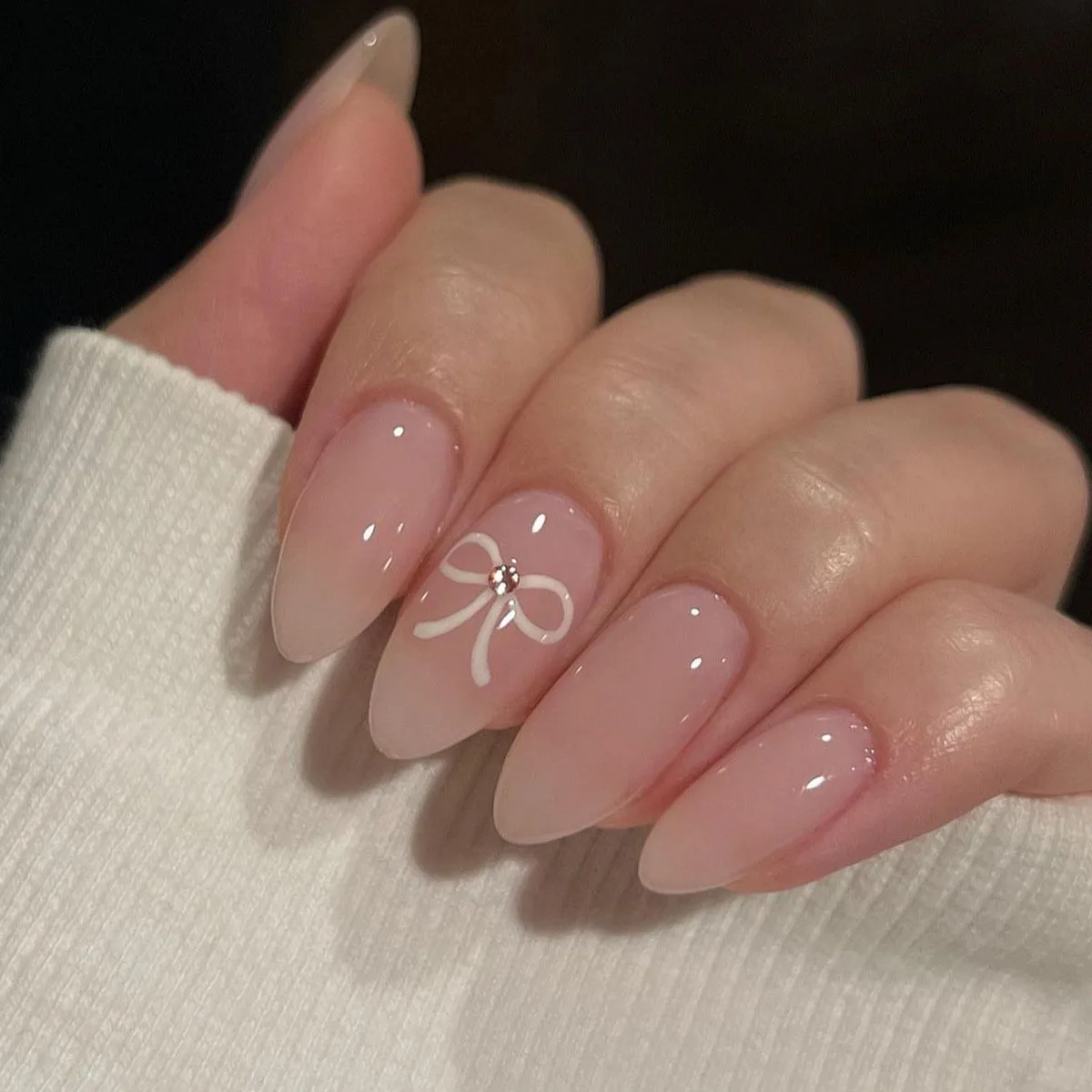 The complete set of 24 long almond shaped pointed nails features a simple white bow and a three-dimensional rhinestone design in