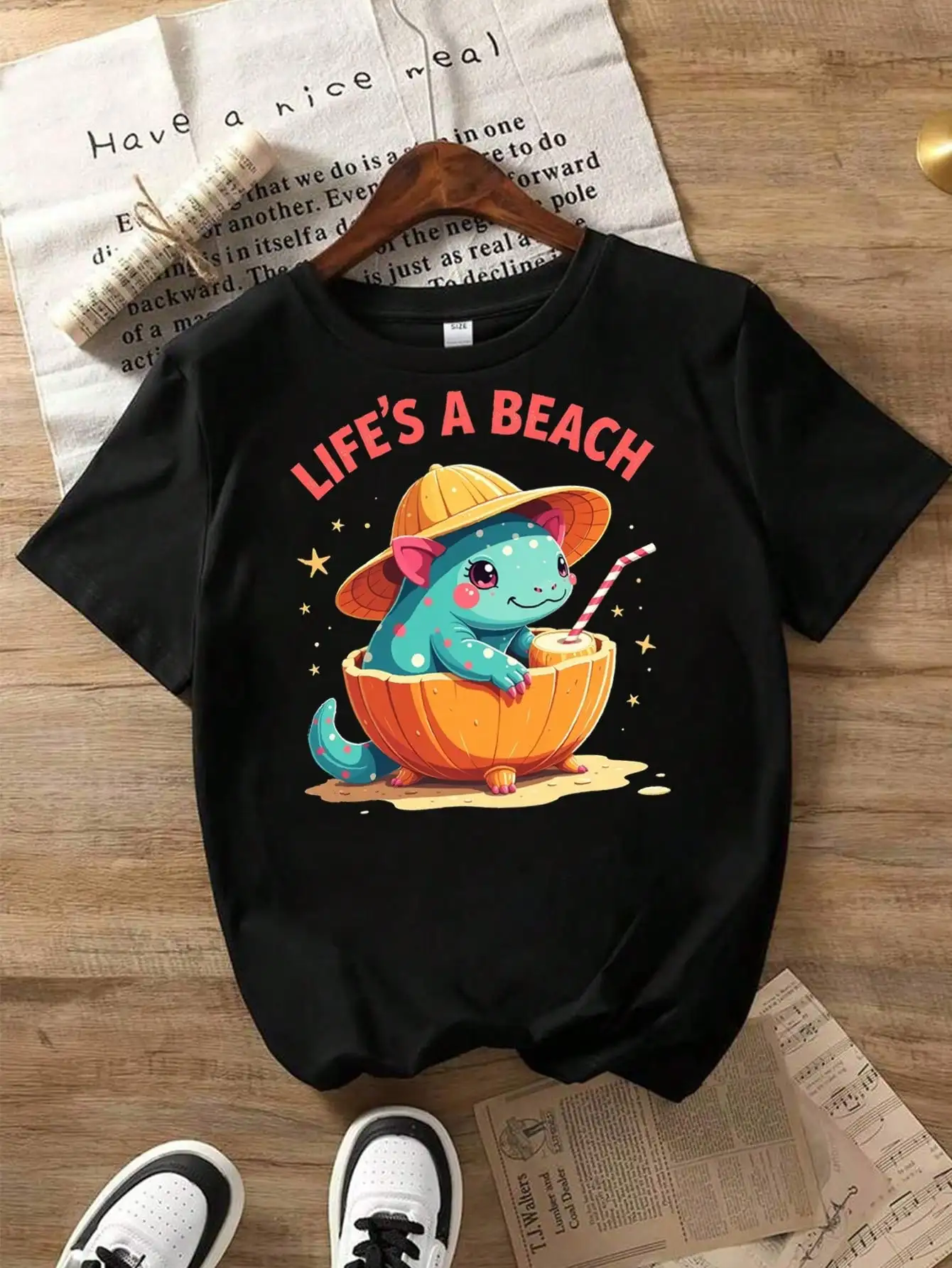 

Cute Mexican Axolotl Fantasy Beach Vibes Cotton T-Shirt, Black Tee With Dino In Orange Hat And Beach Elements