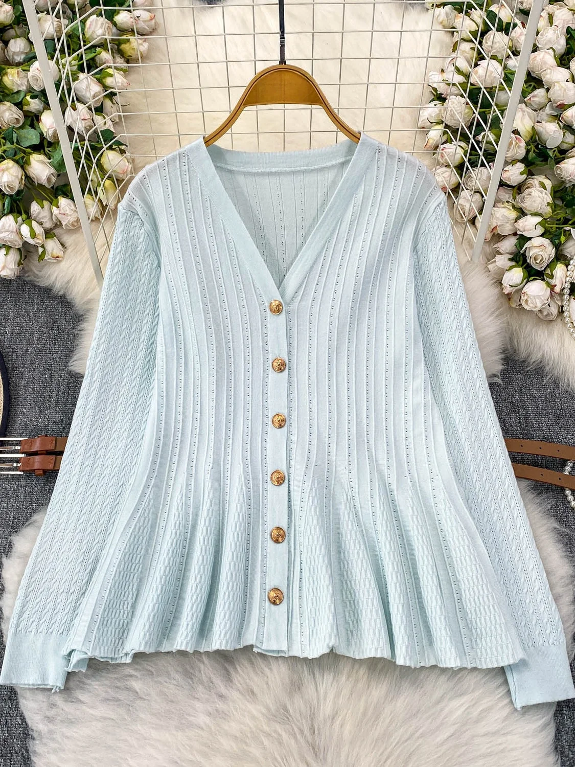 Niebieska dzianinowa bluzka z dekoltem w serek, długim rękawem, ażurowym wzorem, damska, jesienna, elegancka, z paskiem w talii, metalowa, niebieska, delikatny wiatr.