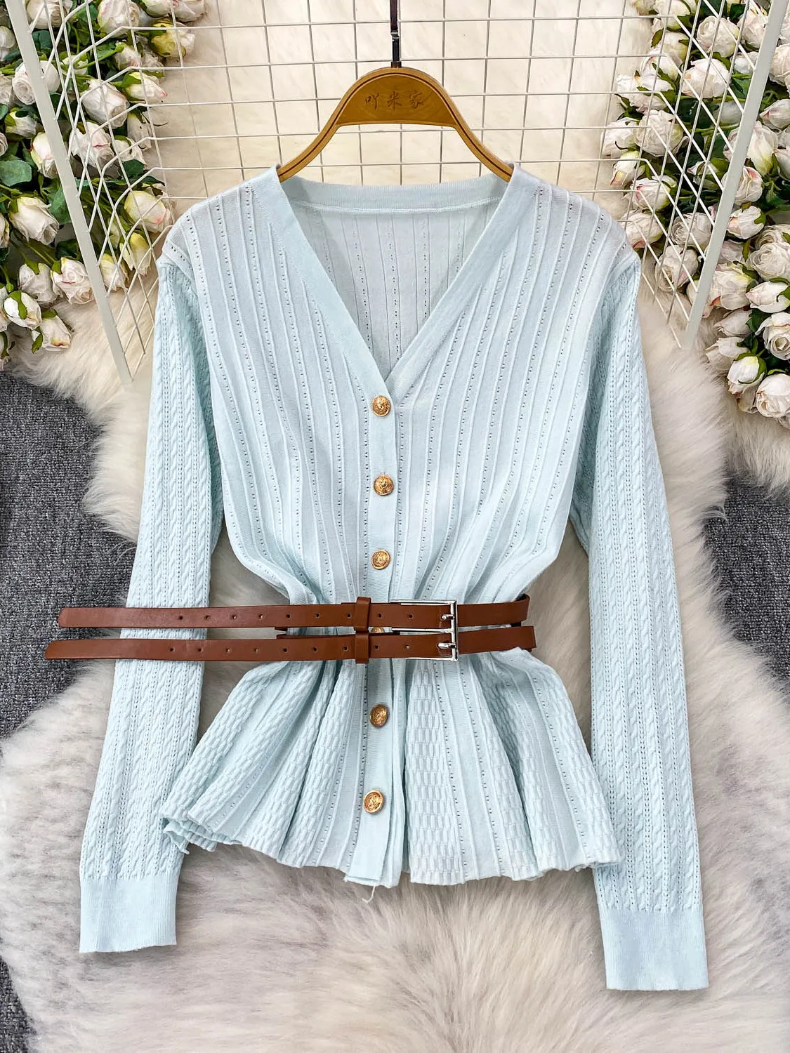 Niebieska dzianinowa bluzka z dekoltem w serek, długim rękawem, ażurowym wzorem, damska, jesienna, elegancka, z paskiem w talii, metalowa, niebieska, delikatny wiatr.