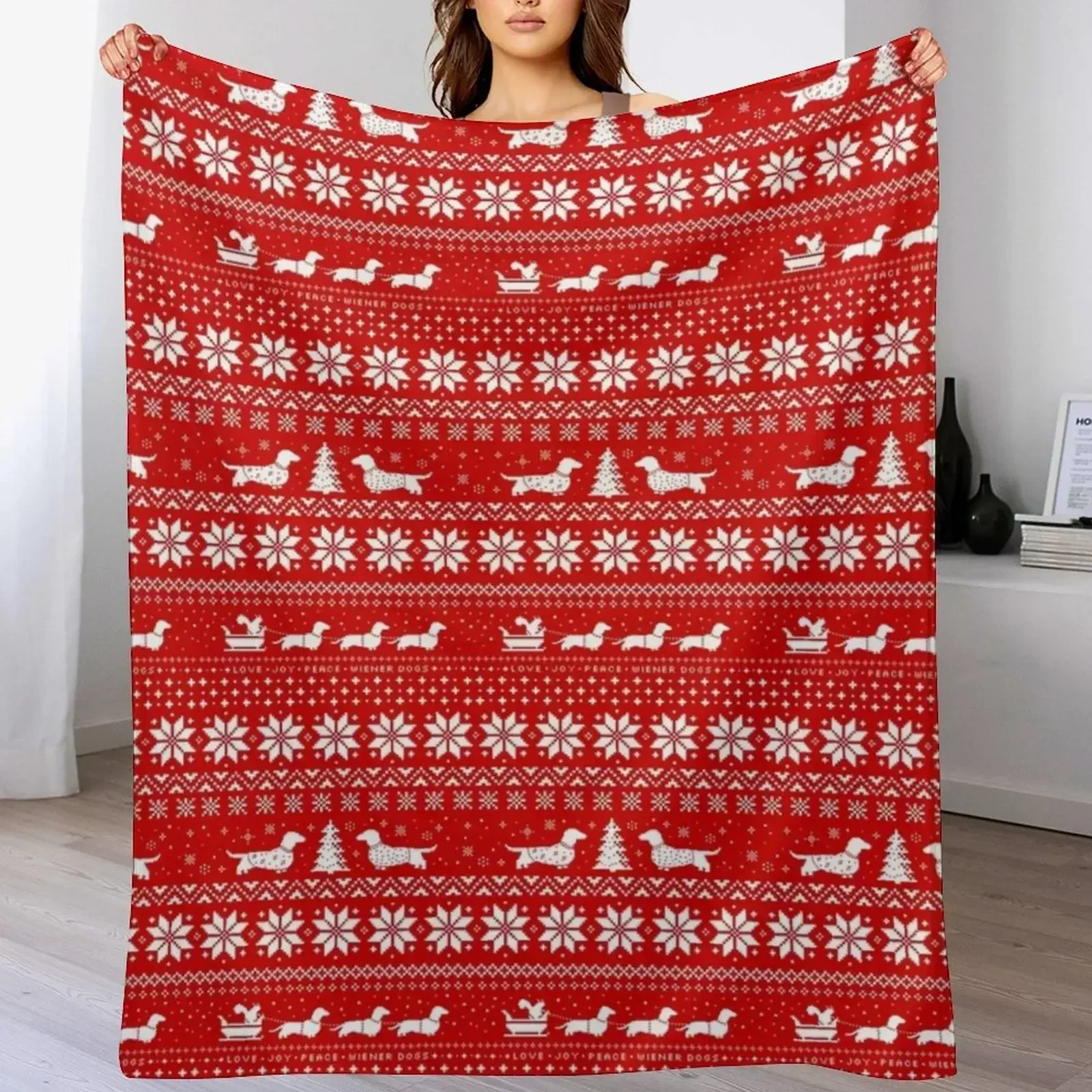 Cozy red throw blanket featuring a white fair-isle Christmas sweater pattern with silhouettes of dachshund dogs and snowflakes draped over a woman sleeping.