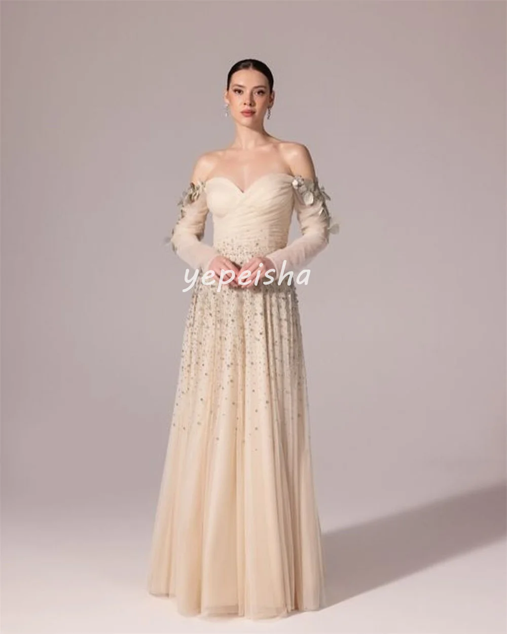 ชุดราตรีทรงเอไลน์แบบเปิดไหล่ ประดับด้วยผ้าทูลล์ระยิบระยับ แต่งดอกไม้ ลูกปัด และเลื่อม ดีไซน์หรูหรา