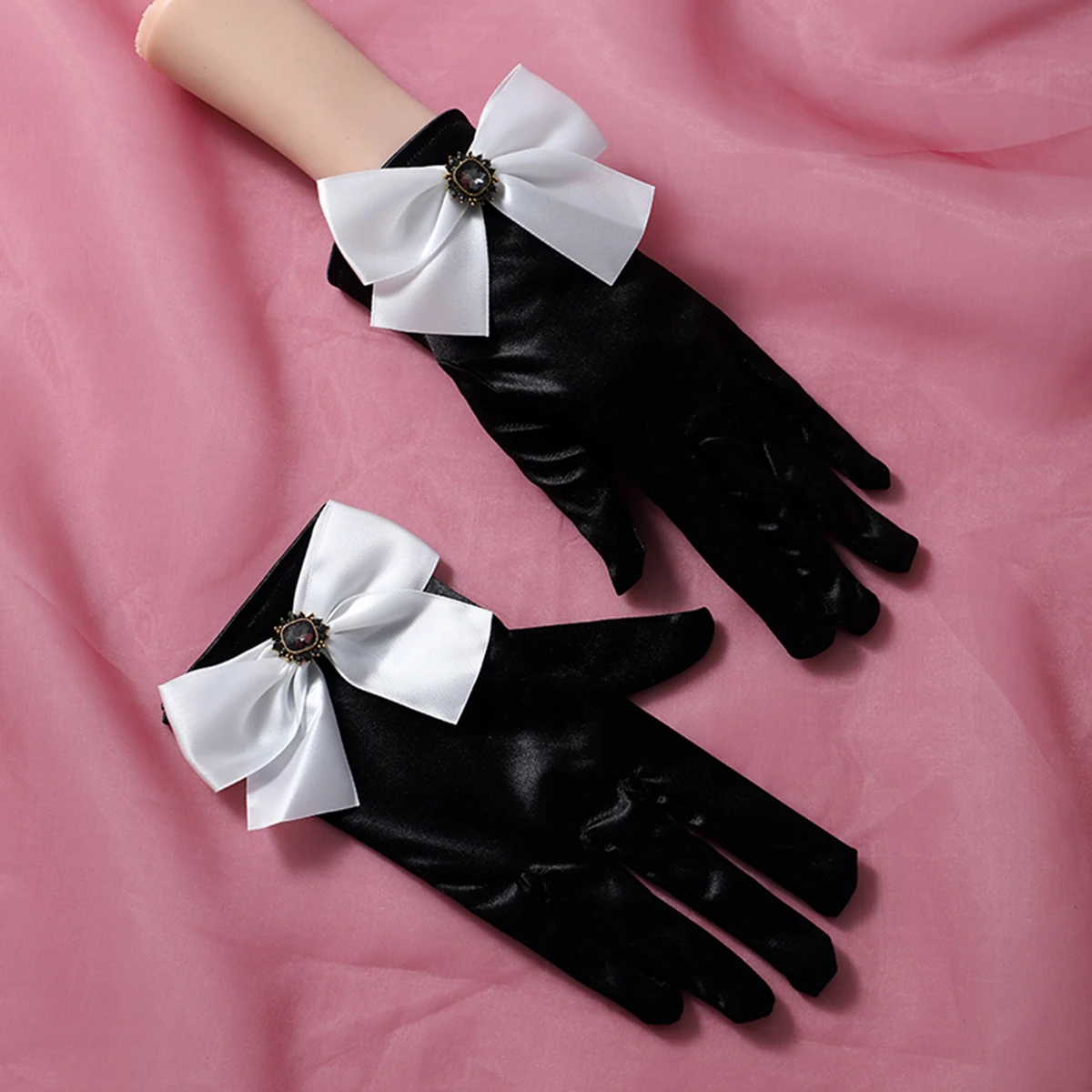 A pair of black wrist length gloves with bow decorations suitable as accessories for bride weddings or women's dances