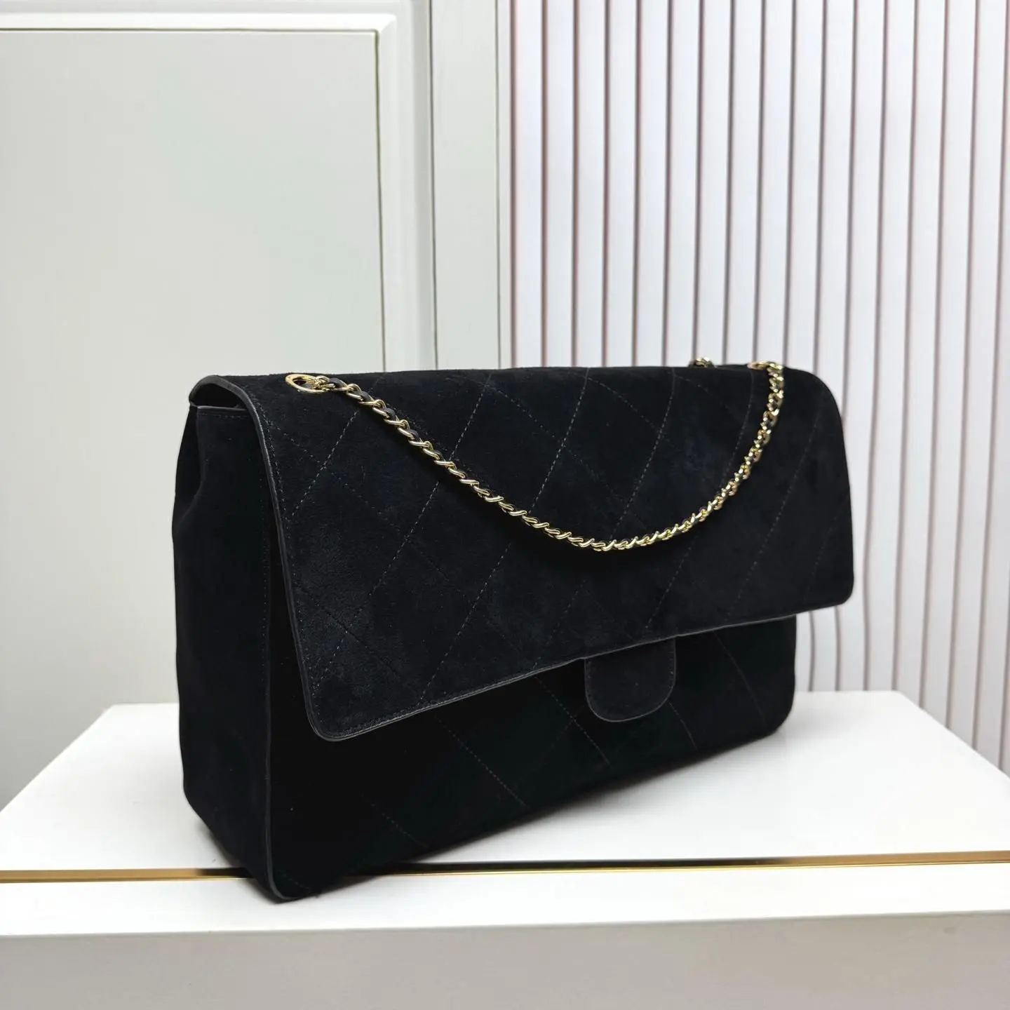 Medium-sized all-black suede crossbody bag, with dense stitching texture, a flap design, and smooth antique brass hardware.