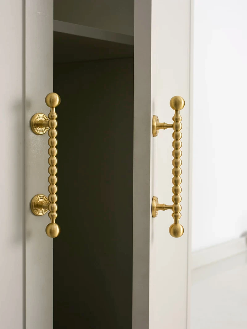 Two beaded handles shown across white cabinet doors