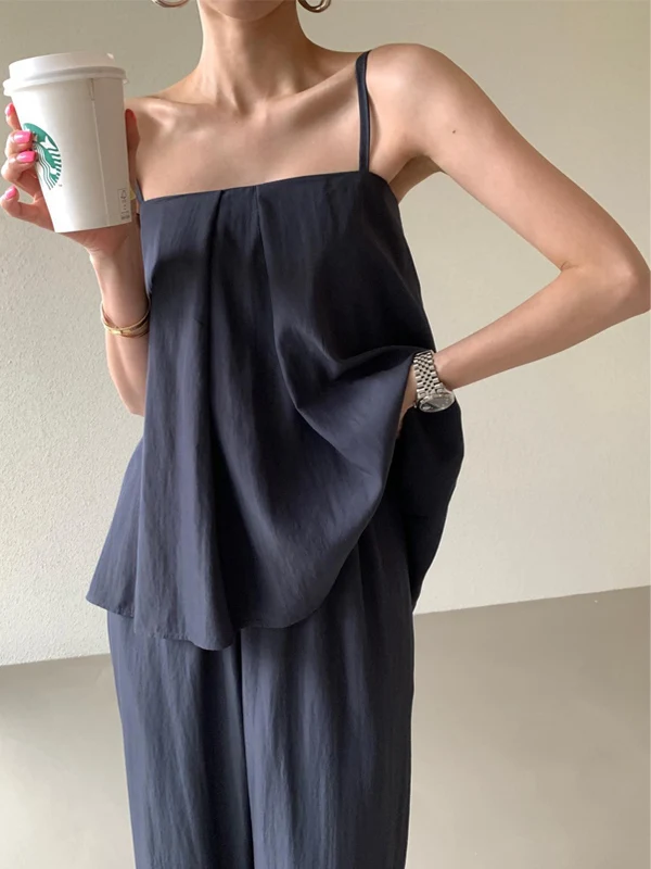 

Ретро-комплект: топ на бретелях с драпировкой и брюки с широкими штанинами на высокой талии. Элегантный модный костюм-двойка для молодых женщин. Лето 2025.