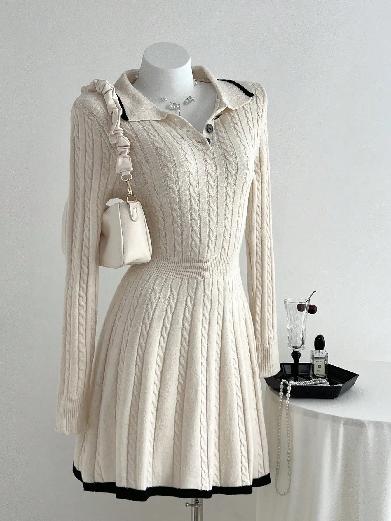 Damska kremowa sukienka swetrowa z długim rękawem, z kołnierzykiem polo, dzianiną w warkocze i czarnymi wykończeniami.