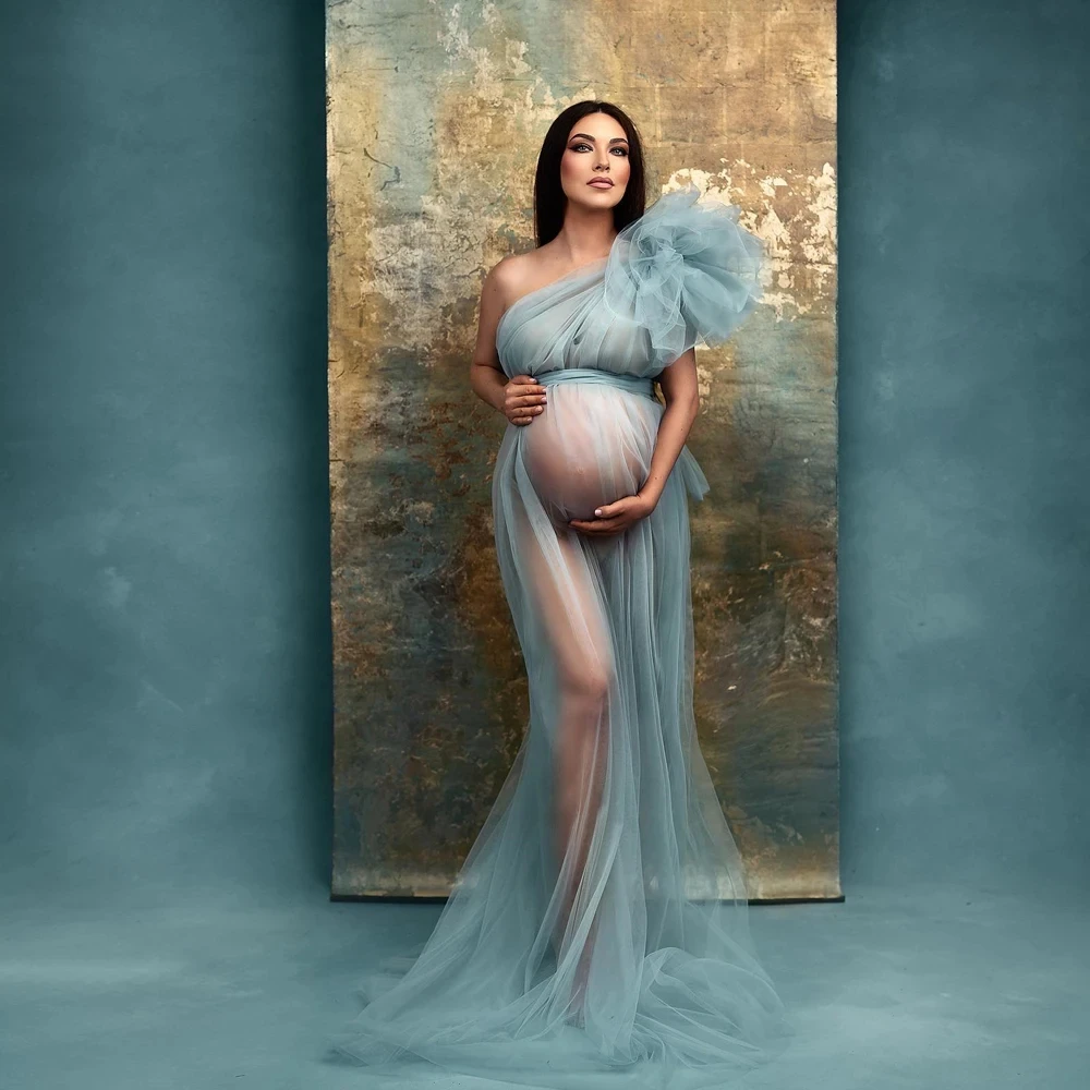 Coloris bleu ciel La robe de grossesse en tulle bleu ciel, portée devant une toile de fond peinte ; le tulle superposé reste transparent sur la jupe.